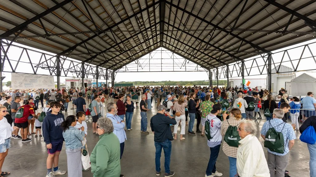 Crowd of people waiting in line inside a large open-air pavilion at an outdoor event.