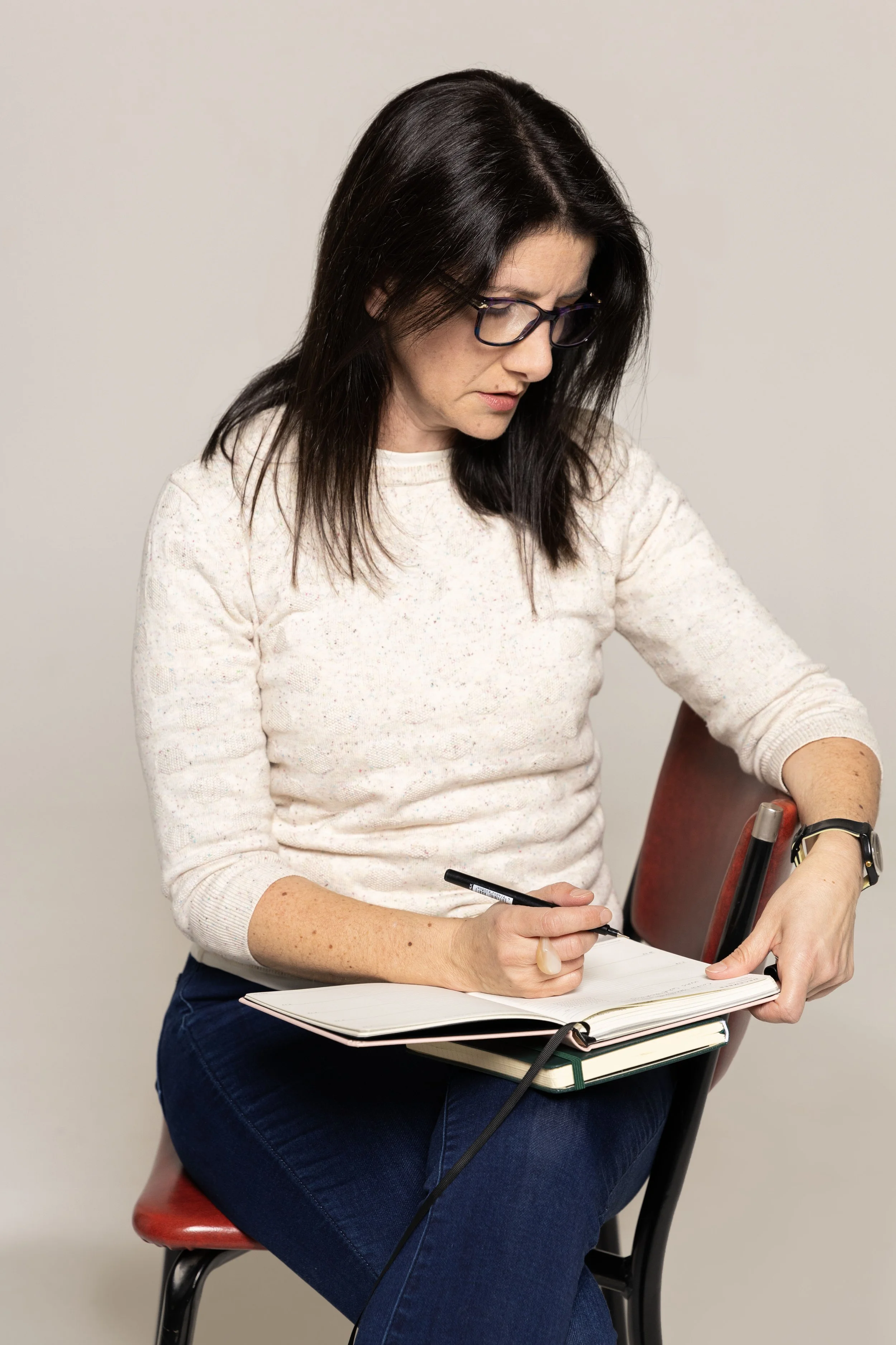 Photo of Patty from Smart Array seated on a red chair, looking down into her notebook, pausing with writing.