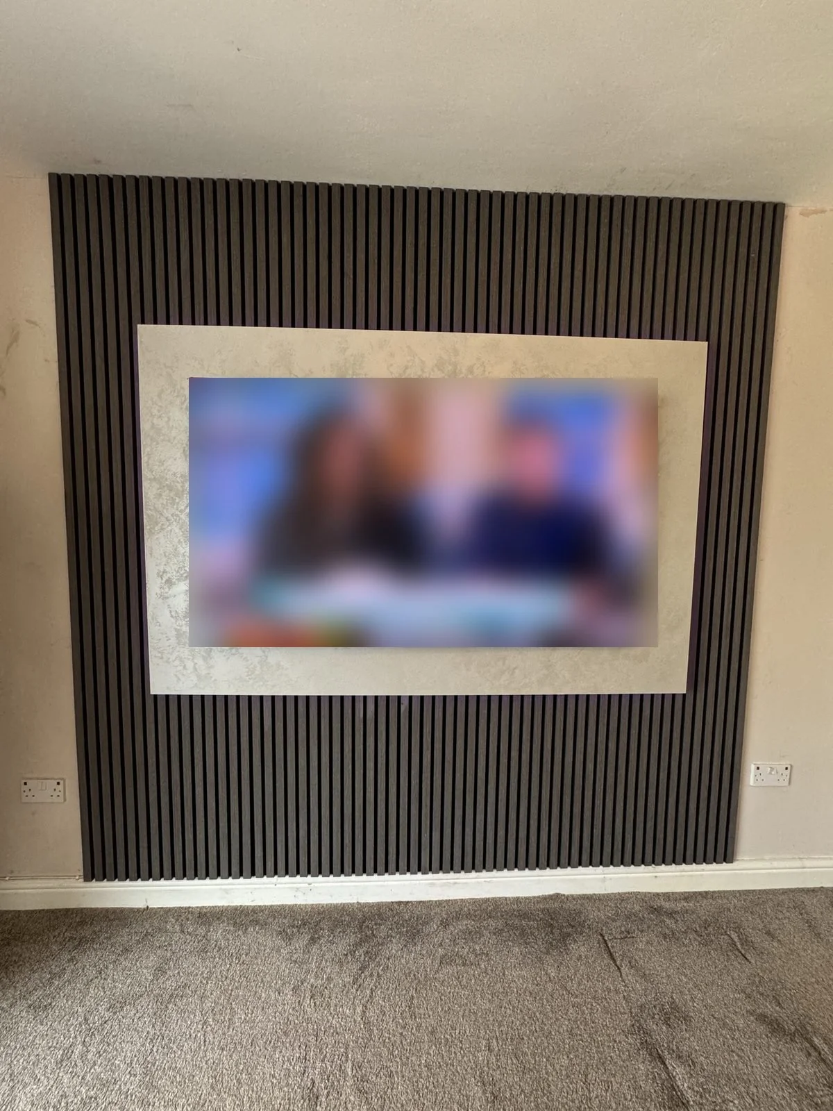 Finished slat panel media wall with stone-effect TV surround, fitted in Manchester