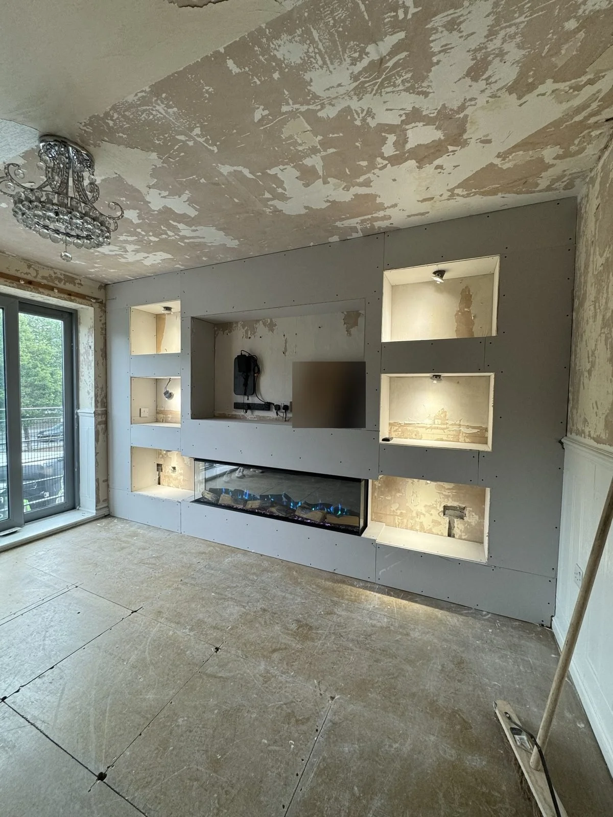 Media wall build before plastering, with lit recessed alcoves either side of the TV and fire