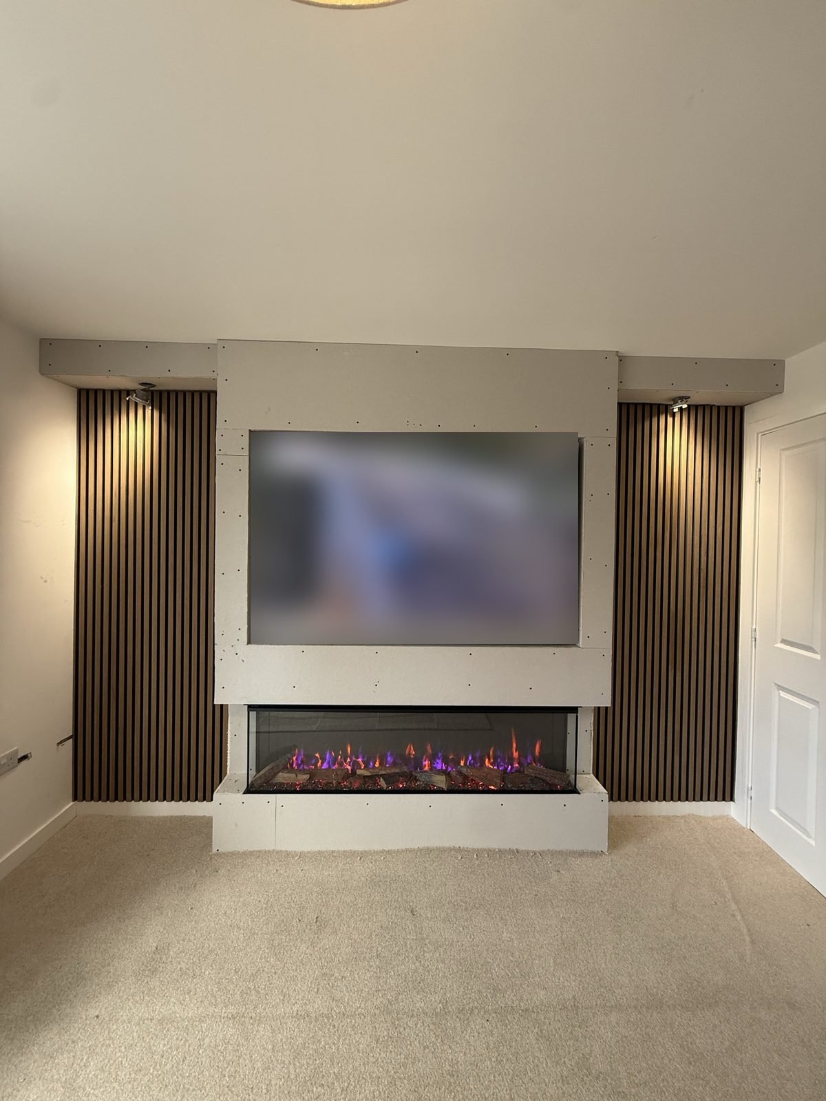 Media wall build before plastering, with TV recess, slat panel alcoves either side and an electric fire