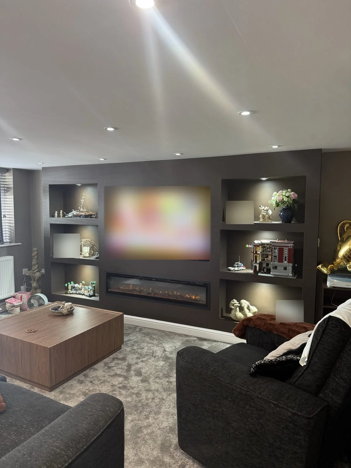 Finished dark grey media wall with lit display shelves either side of the TV and a long electric fire