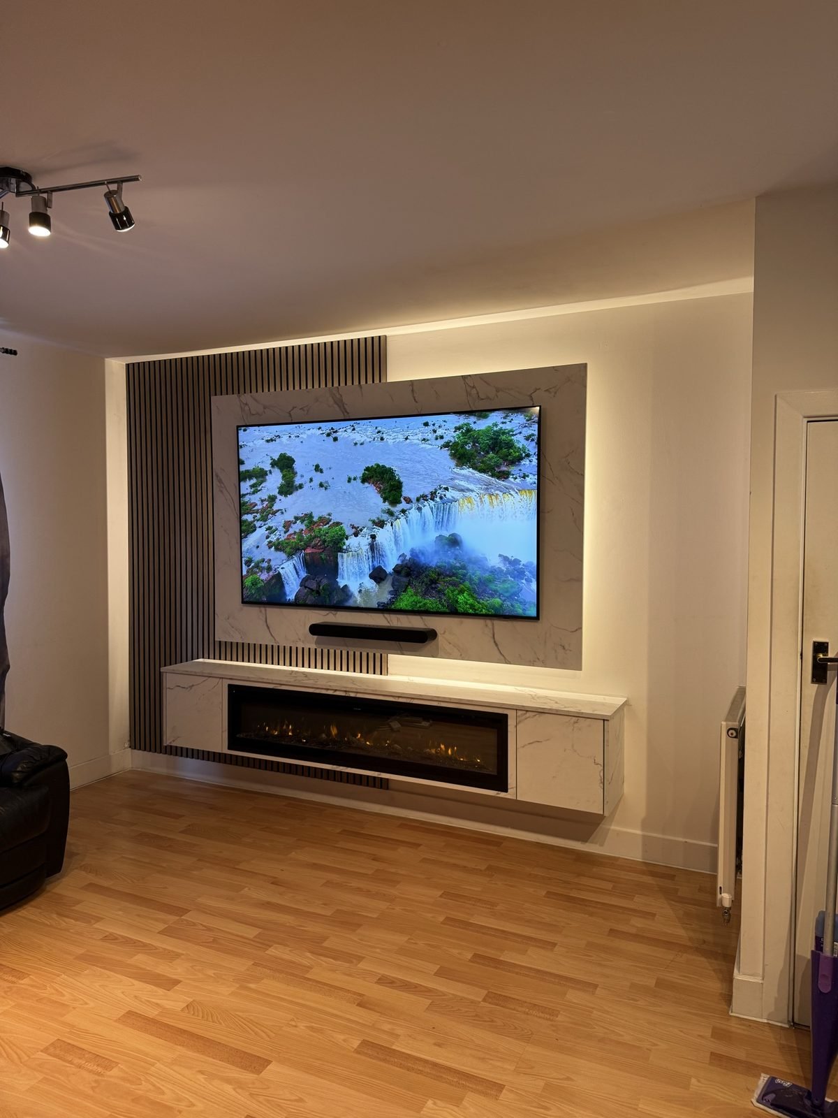 White and grey media wall with a stone-effect TV panel, slat detail and a white floating unit with electric fire