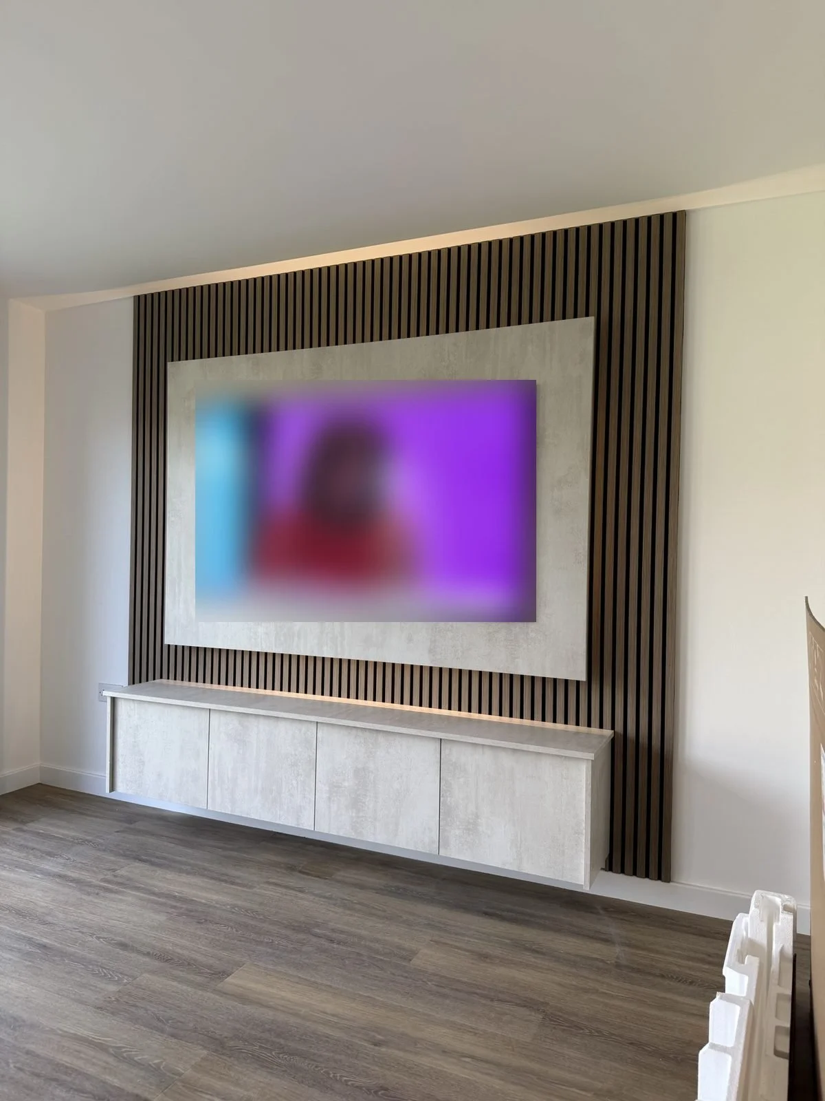 Wood slat panel media wall framing a TV, with a white floating unit underneath
