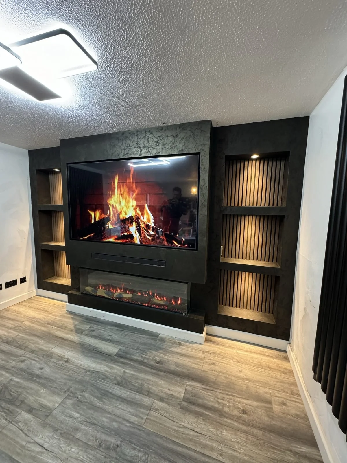 Finished dark media wall with built-in electric fire and lit slat panel alcoves