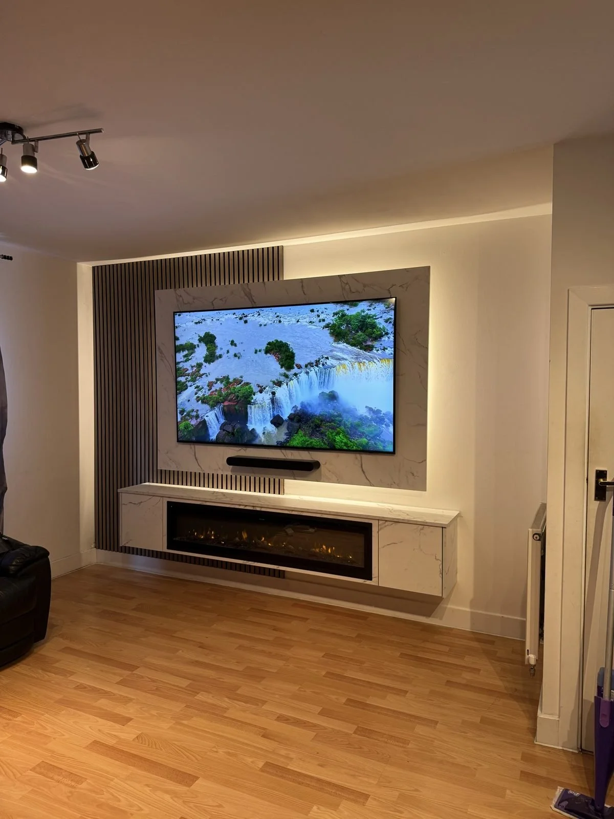 White and grey media wall with a stone-effect TV panel, slat detail and a white floating unit with electric fire