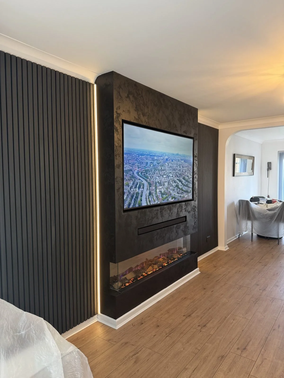 Dark textured media wall with recessed TV, three-sided electric fire and black slat panelling