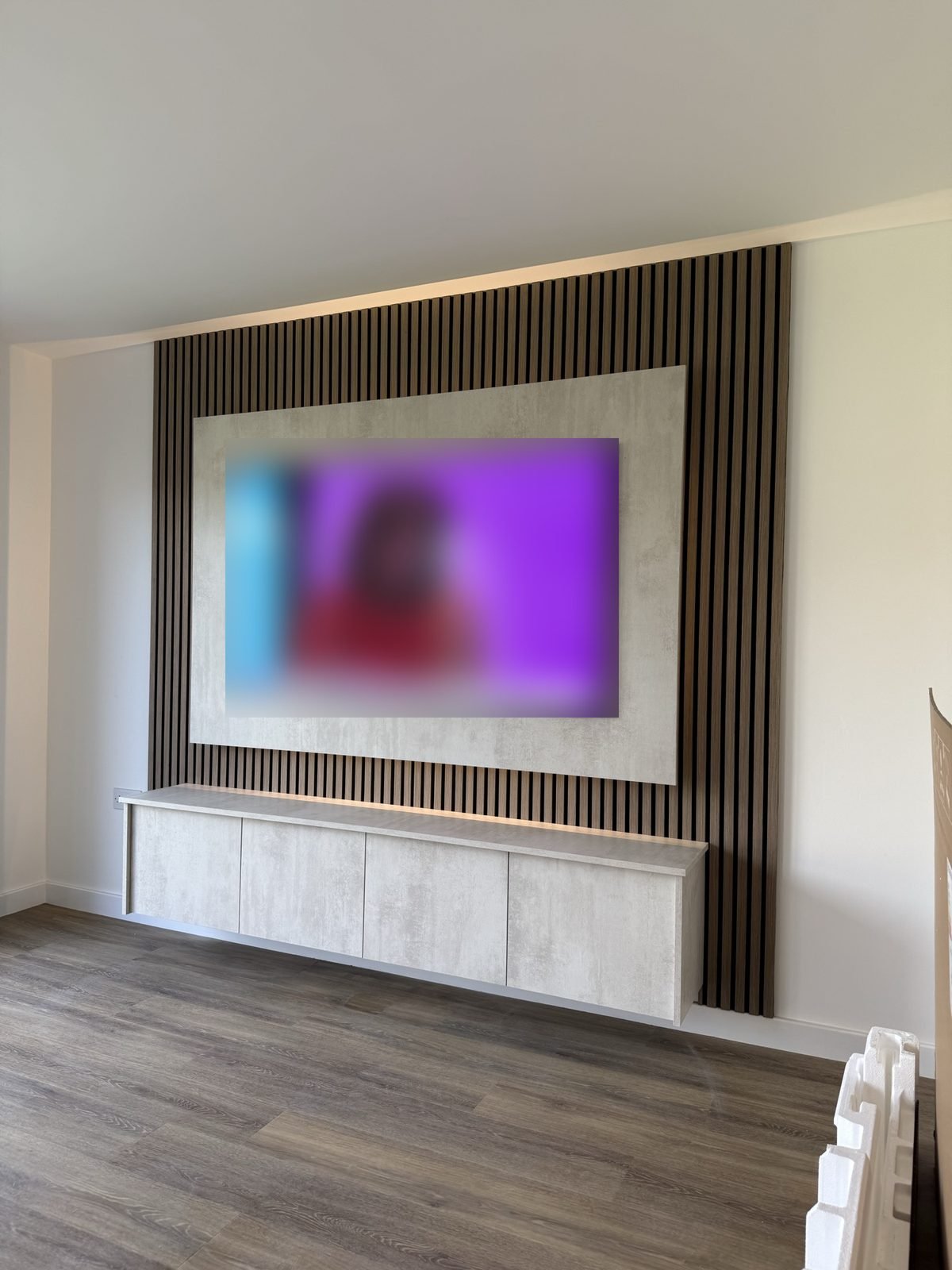 Wood slat panel media wall framing a TV, with a white floating unit underneath