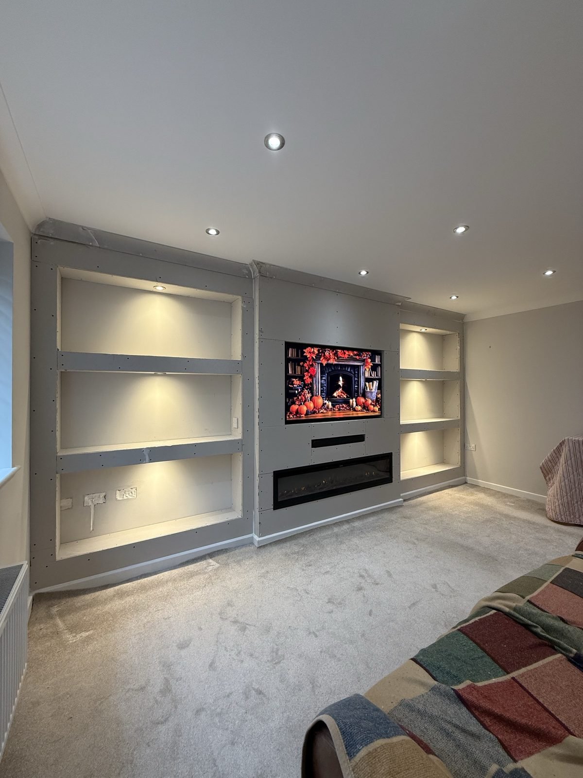 Media wall build before plastering, with lit recessed shelving alcoves either side of the TV and electric fire