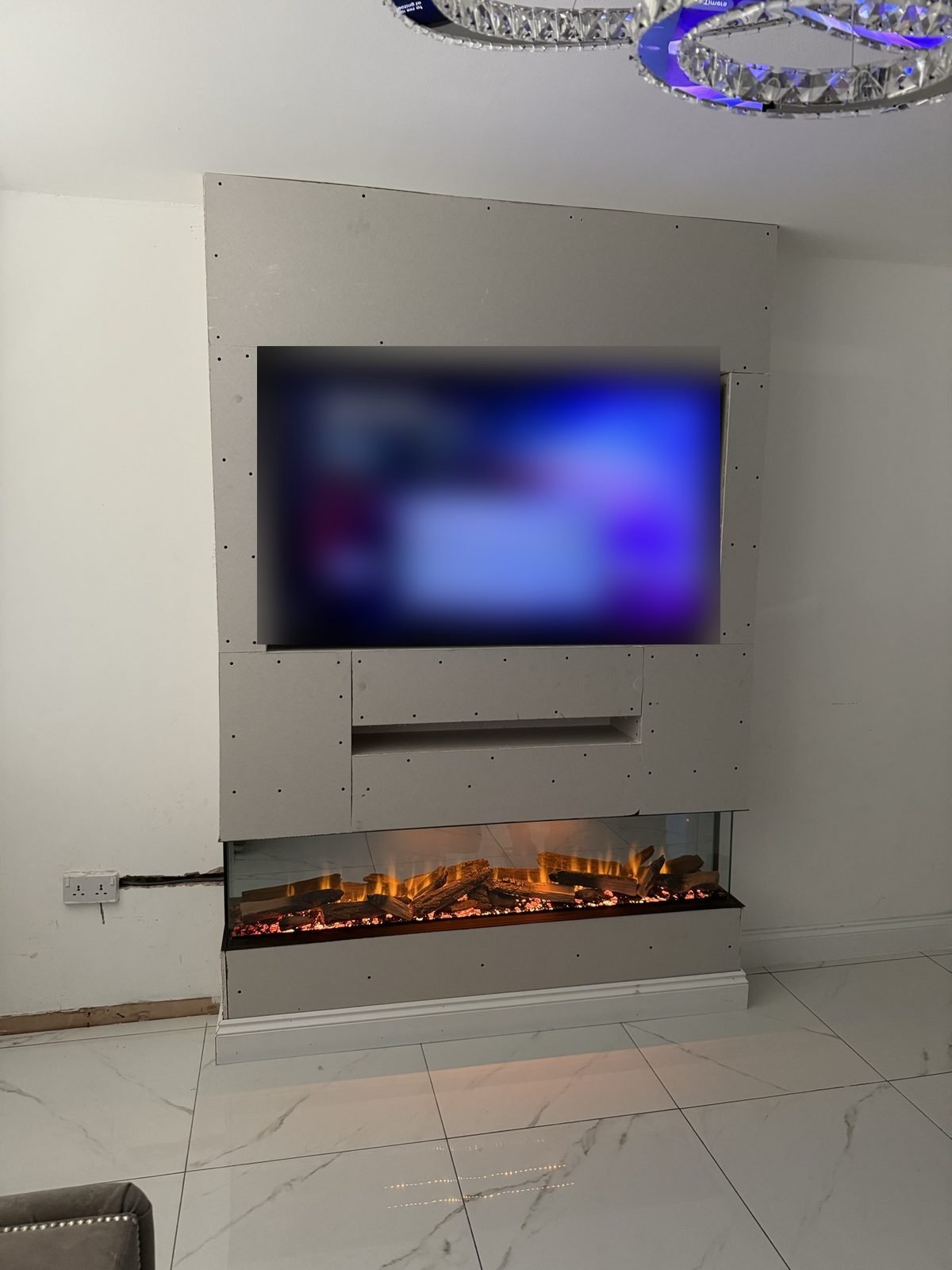 Boarded chimney-breast media wall before plastering, with TV and electric fire, at a Manchester job