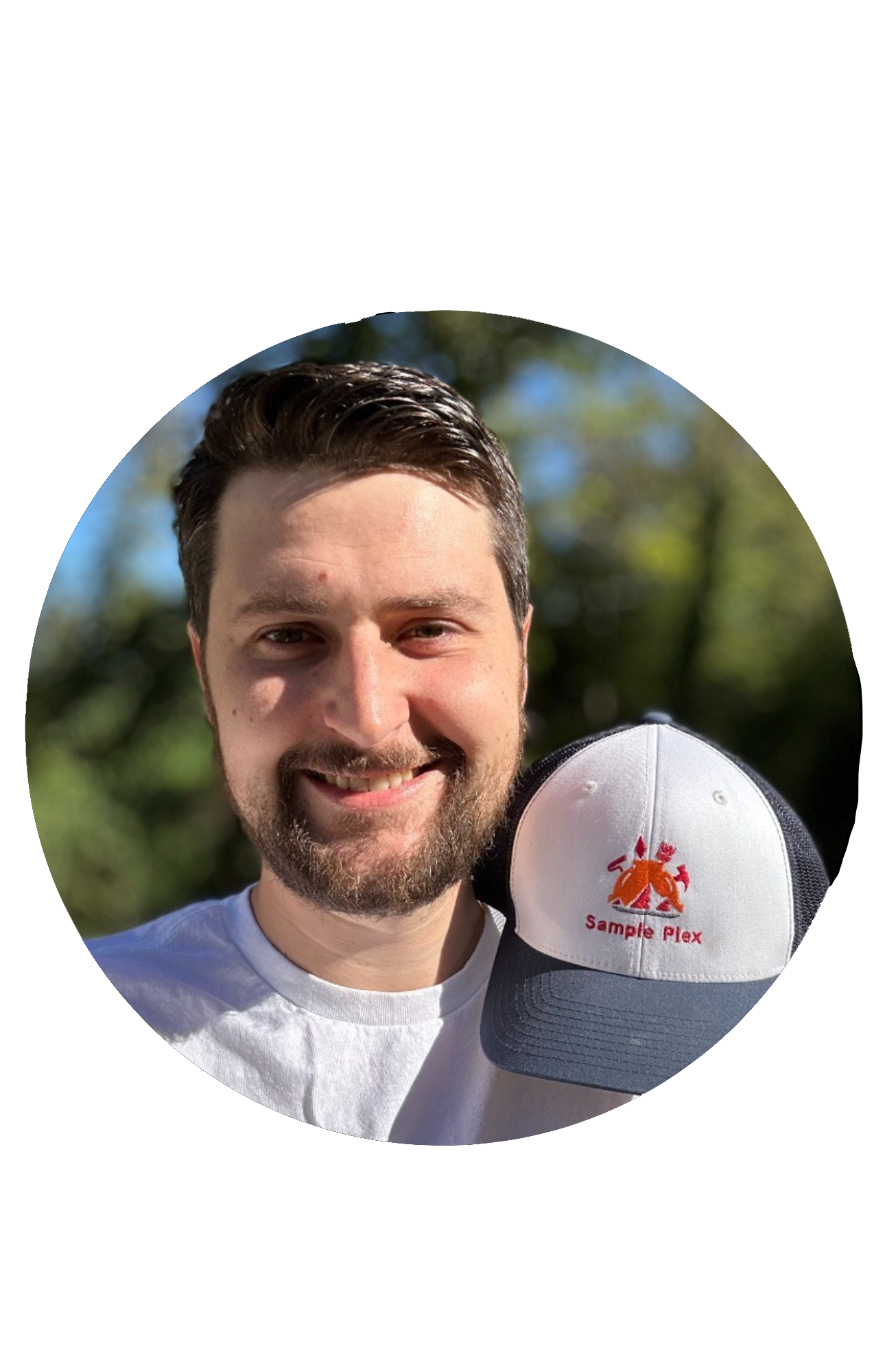 A smiling man with dark hair and a beard holding a white and gray cap with a red logo and the words 'Sample Plex' on it, outdoors with trees and a blue sky in the background.