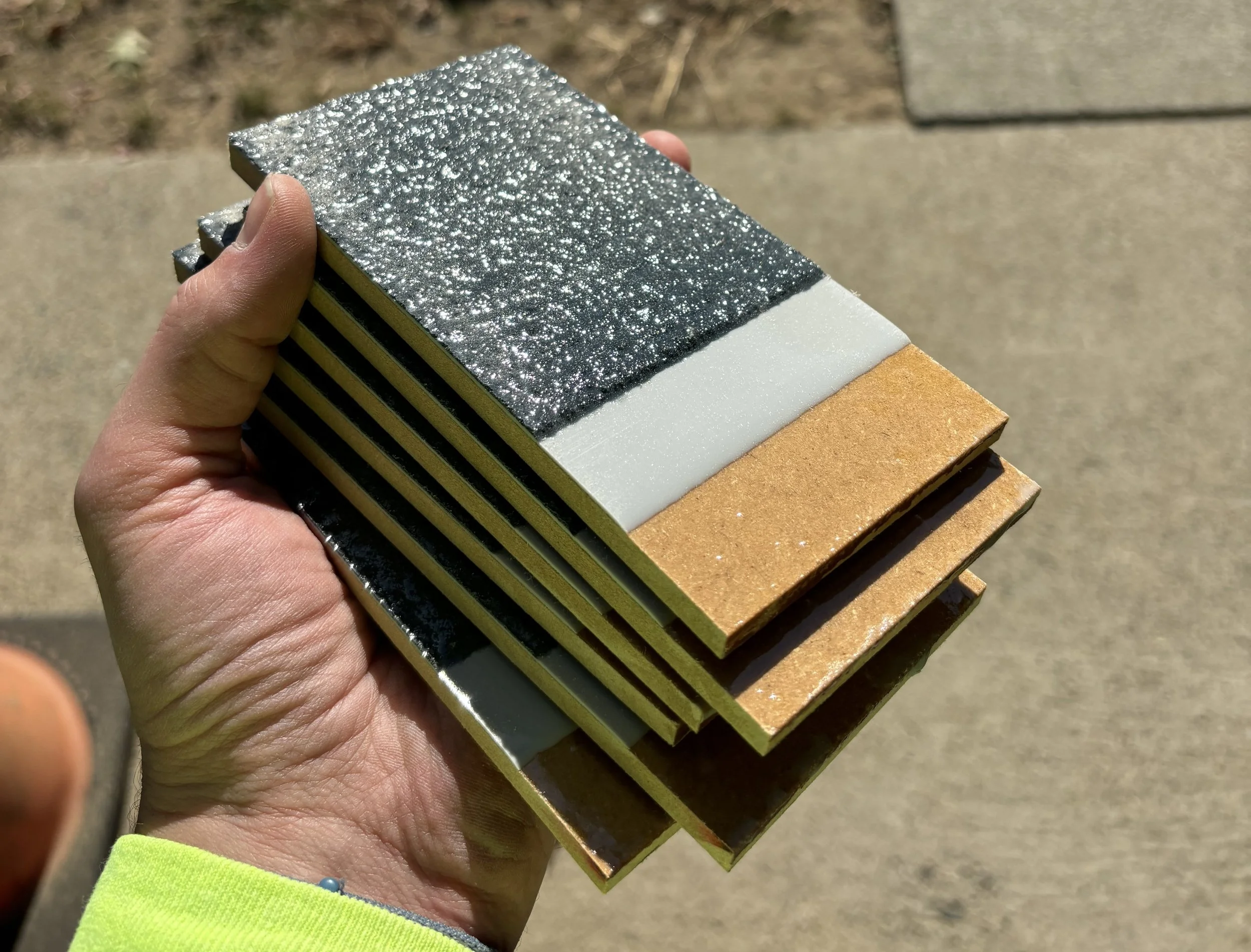 A hand holding several waterproofing samples that are stepped back showing the mdf board, a light gray and then a dark grey coating.