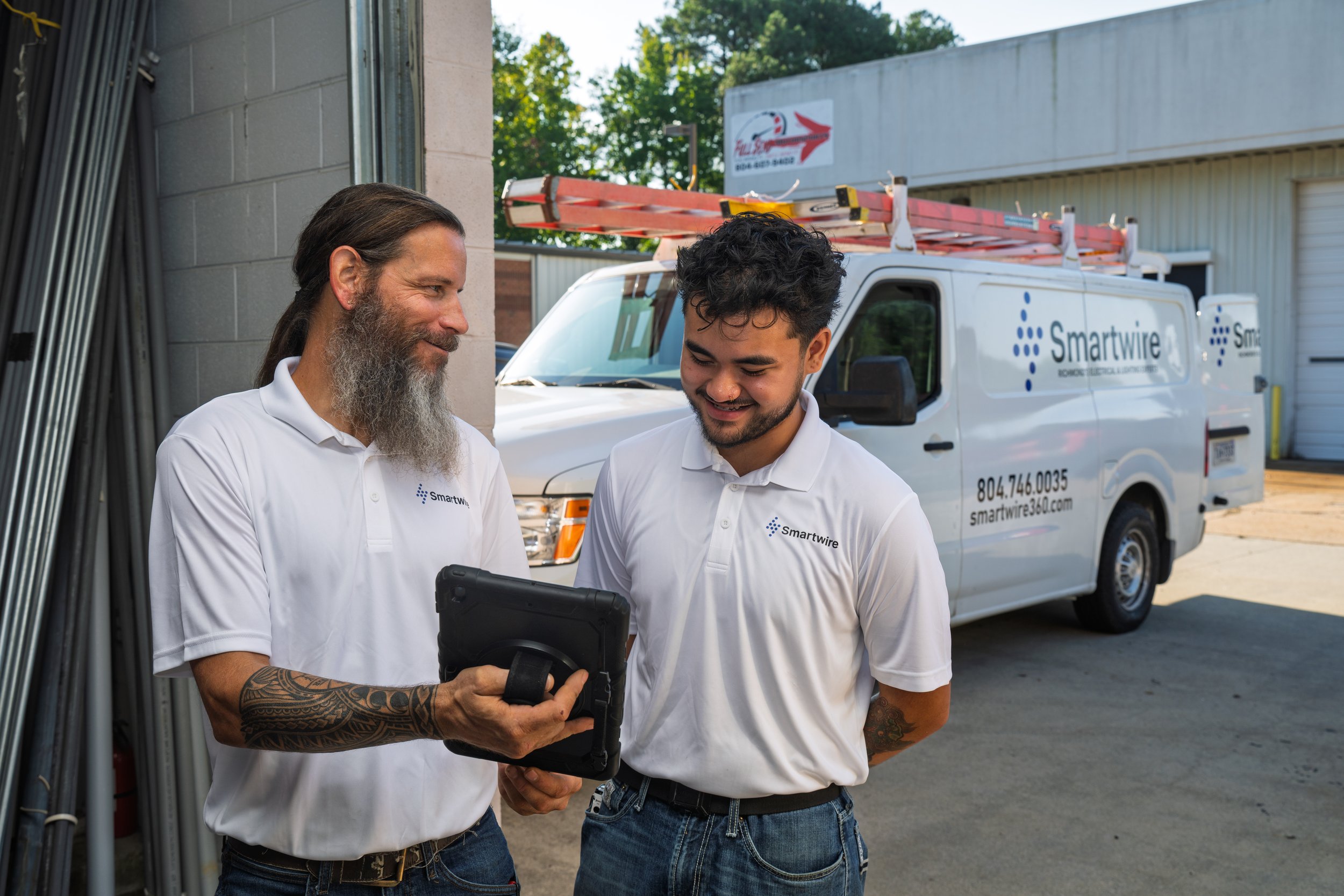 A white delivery van with the 'Smartwire' logo is parked on the street in front of a modern building with large windows, trees, and bushes.