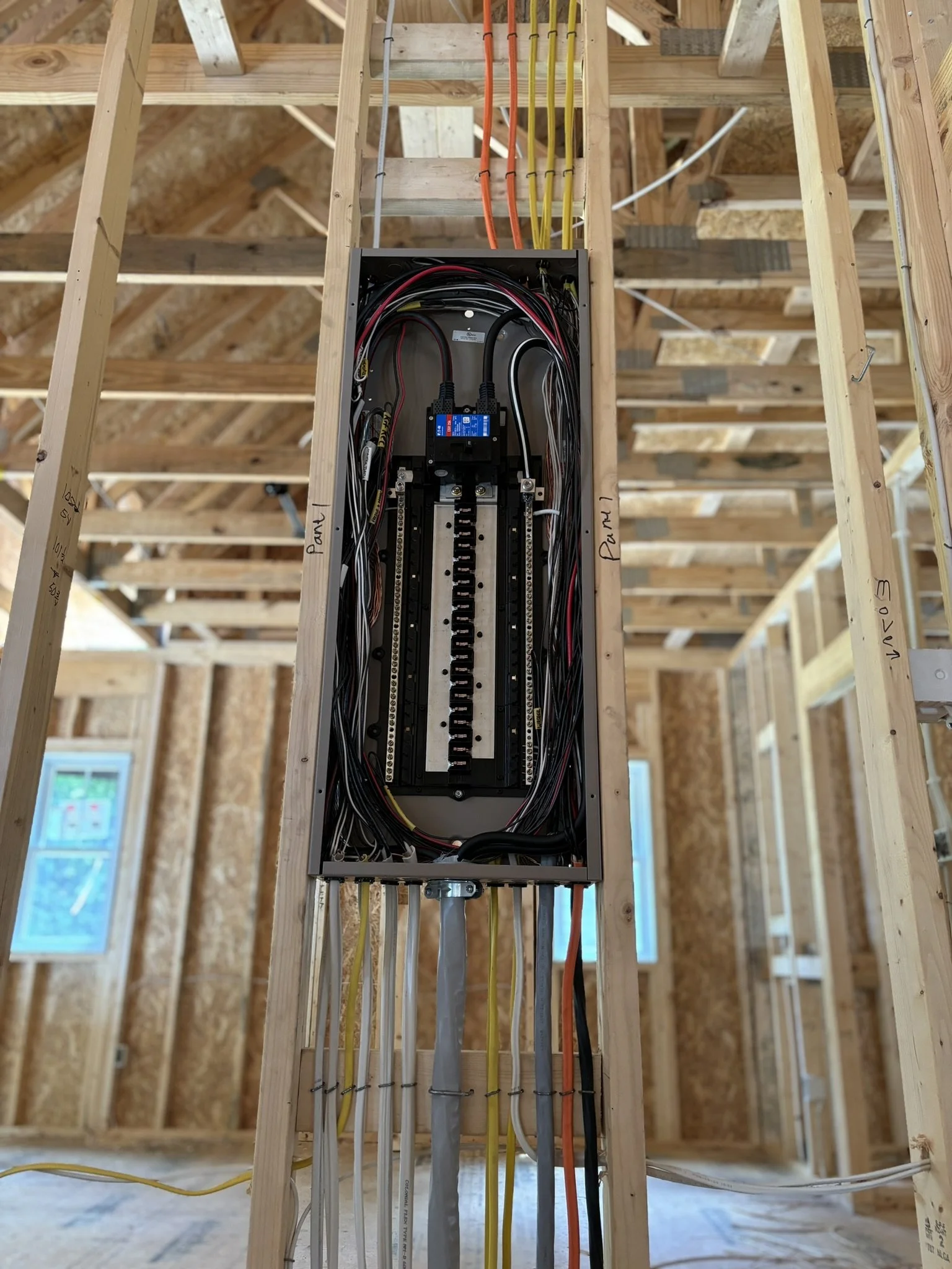 Electrical panel installed within a wooden framing of a building under construction, with colorful electrical wires connected inside.