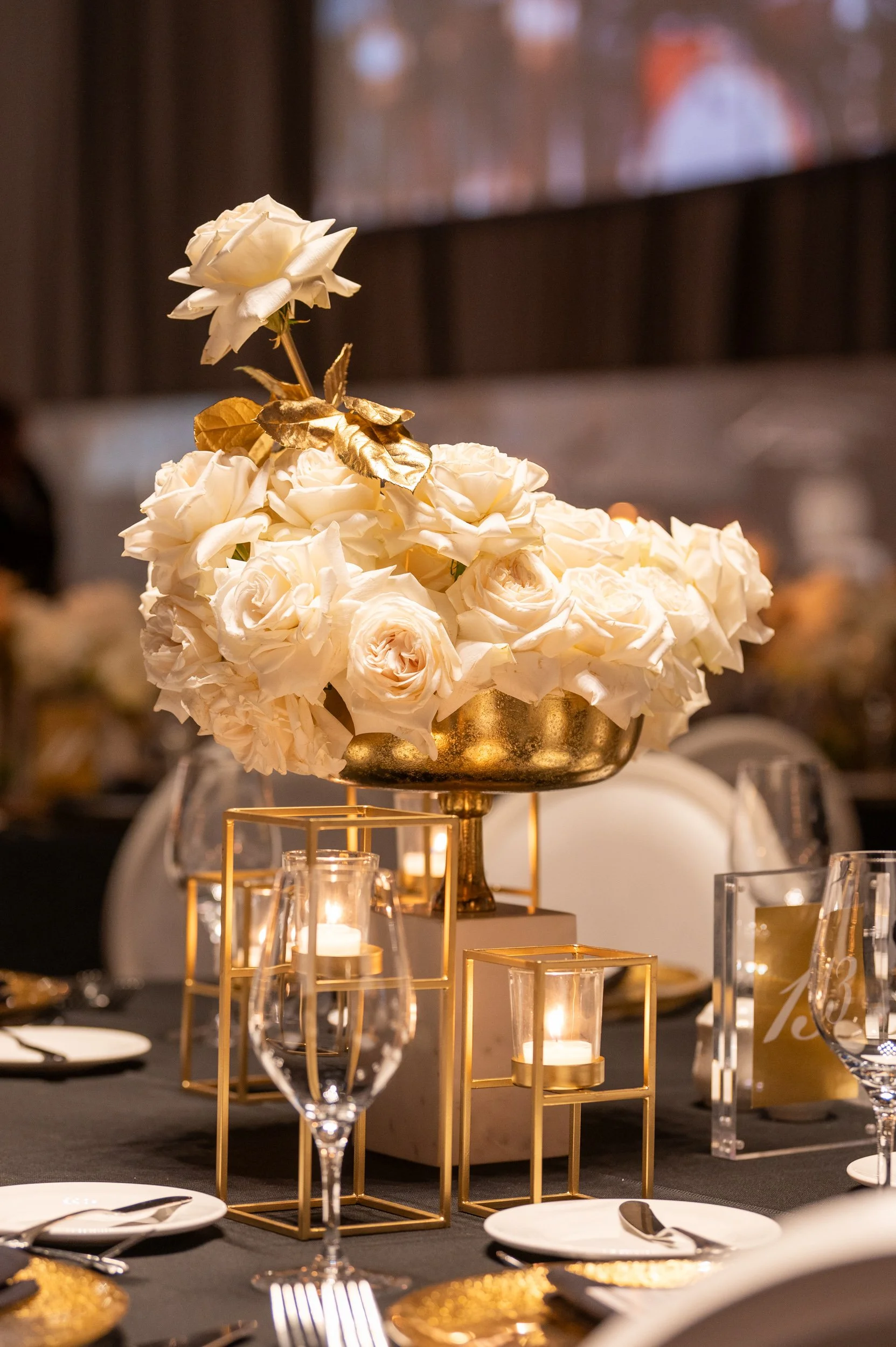Elegant table centerpiece with white roses, gold accents, and candle holders at a formal event.