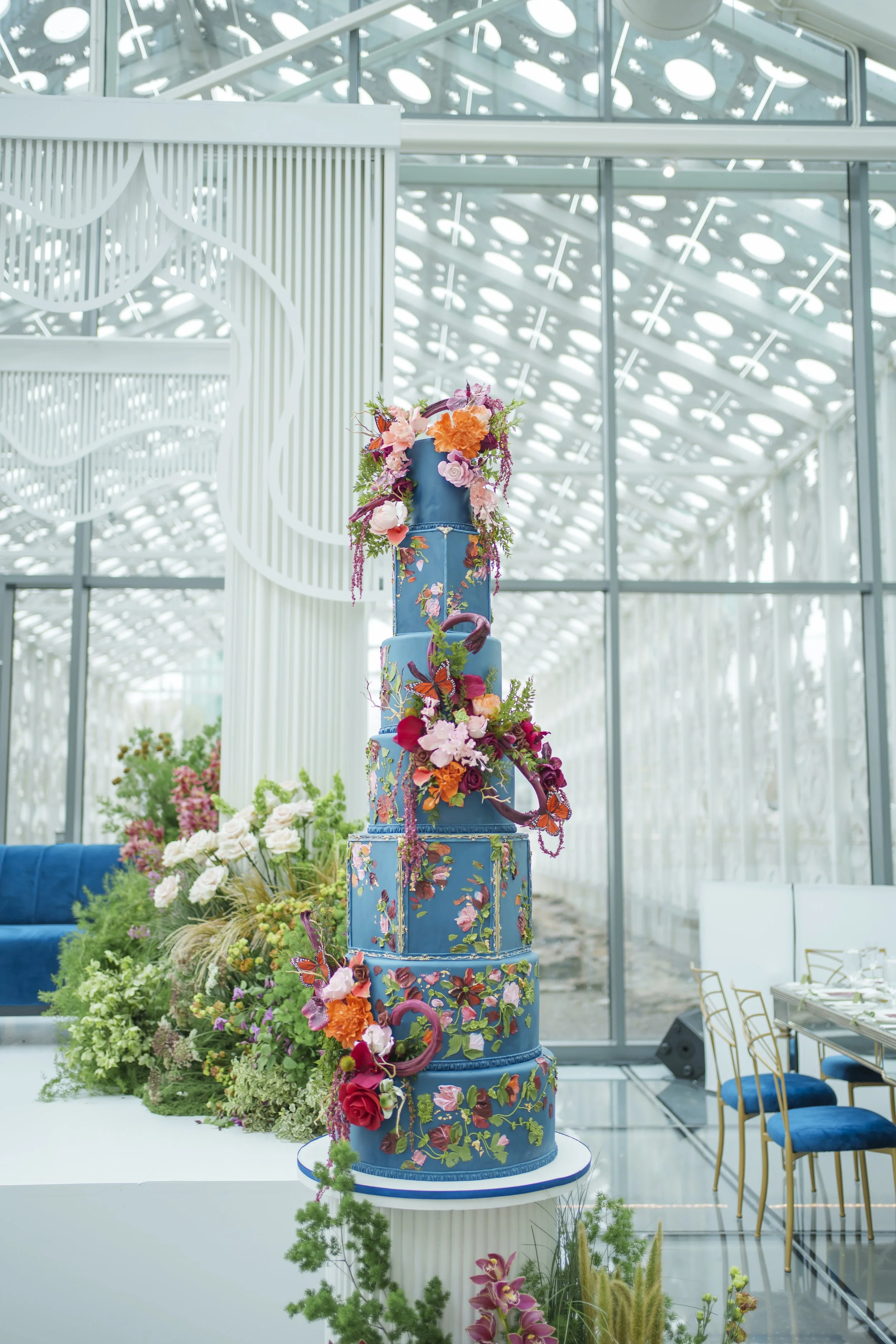 Tall blue wedding cake decorated with red and orange flowers in the glass pavilion at Hotel X Toronto