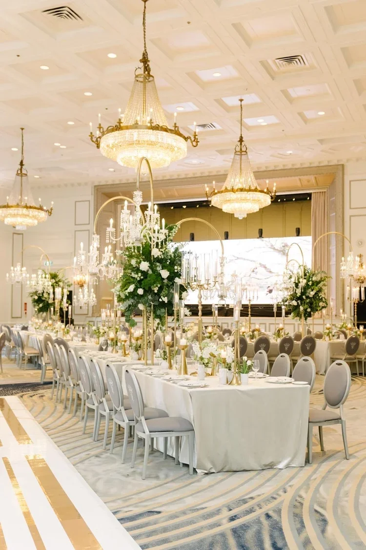 Luxurious banquet hall with elegant chandeliers, tall floral centerpieces, and neatly arranged tables set for a formal event.