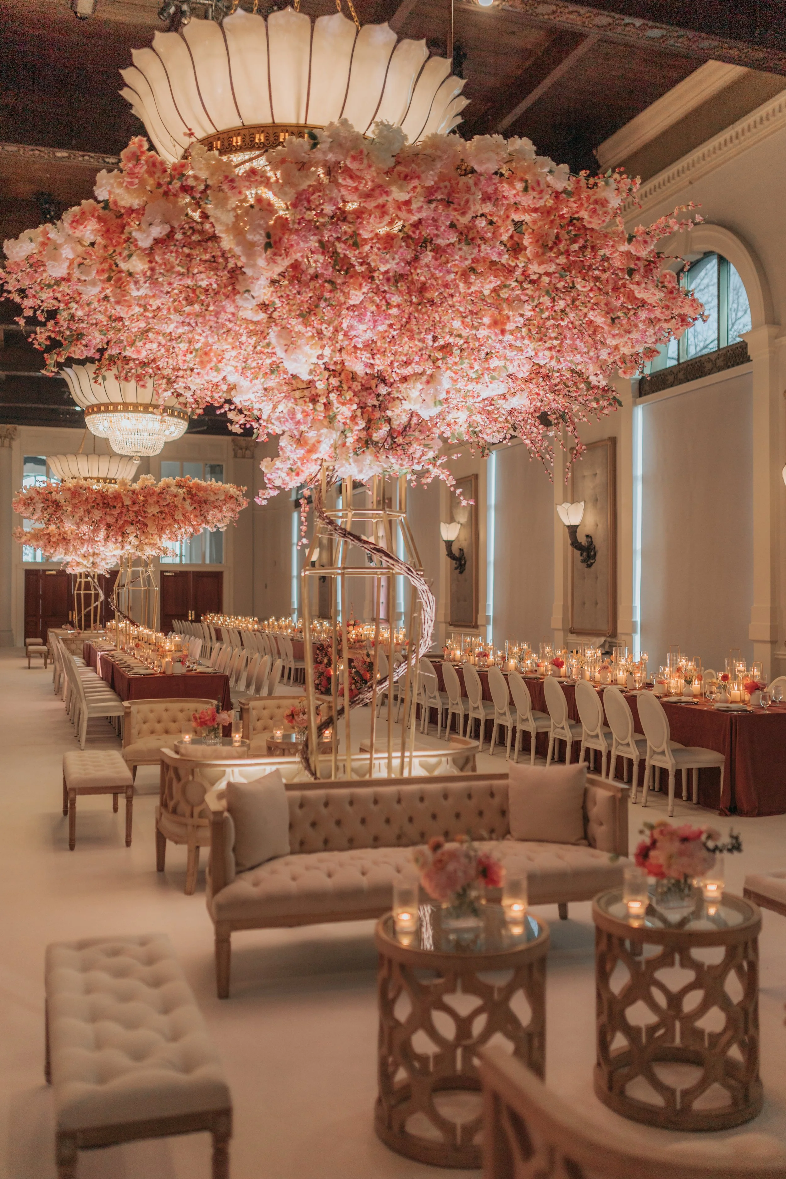 Elegant banquet hall decorated with pink and white cherry blossom trees, chandeliers, and long tables set for a celebration.