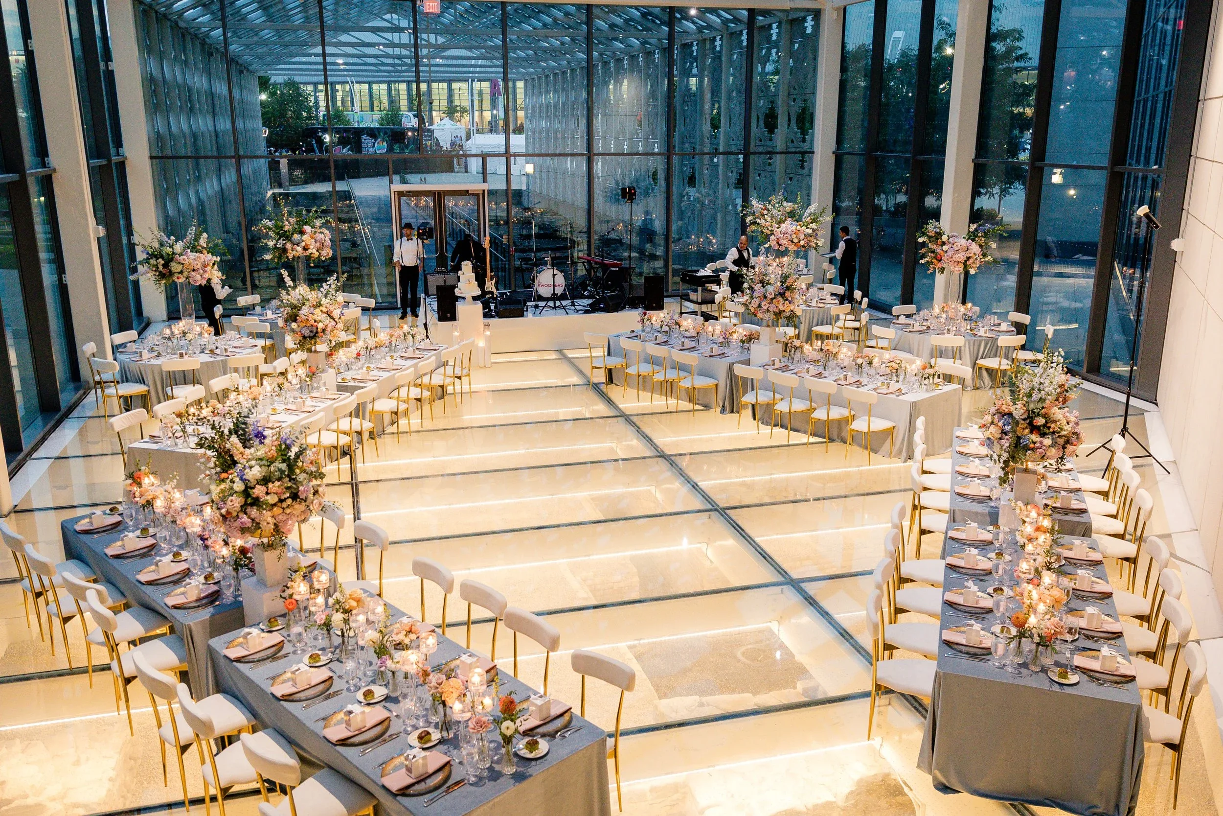 Elegant banquet hall decorated with floral centerpieces and set tables for a wedding or special event, with a stage and large glass windows.