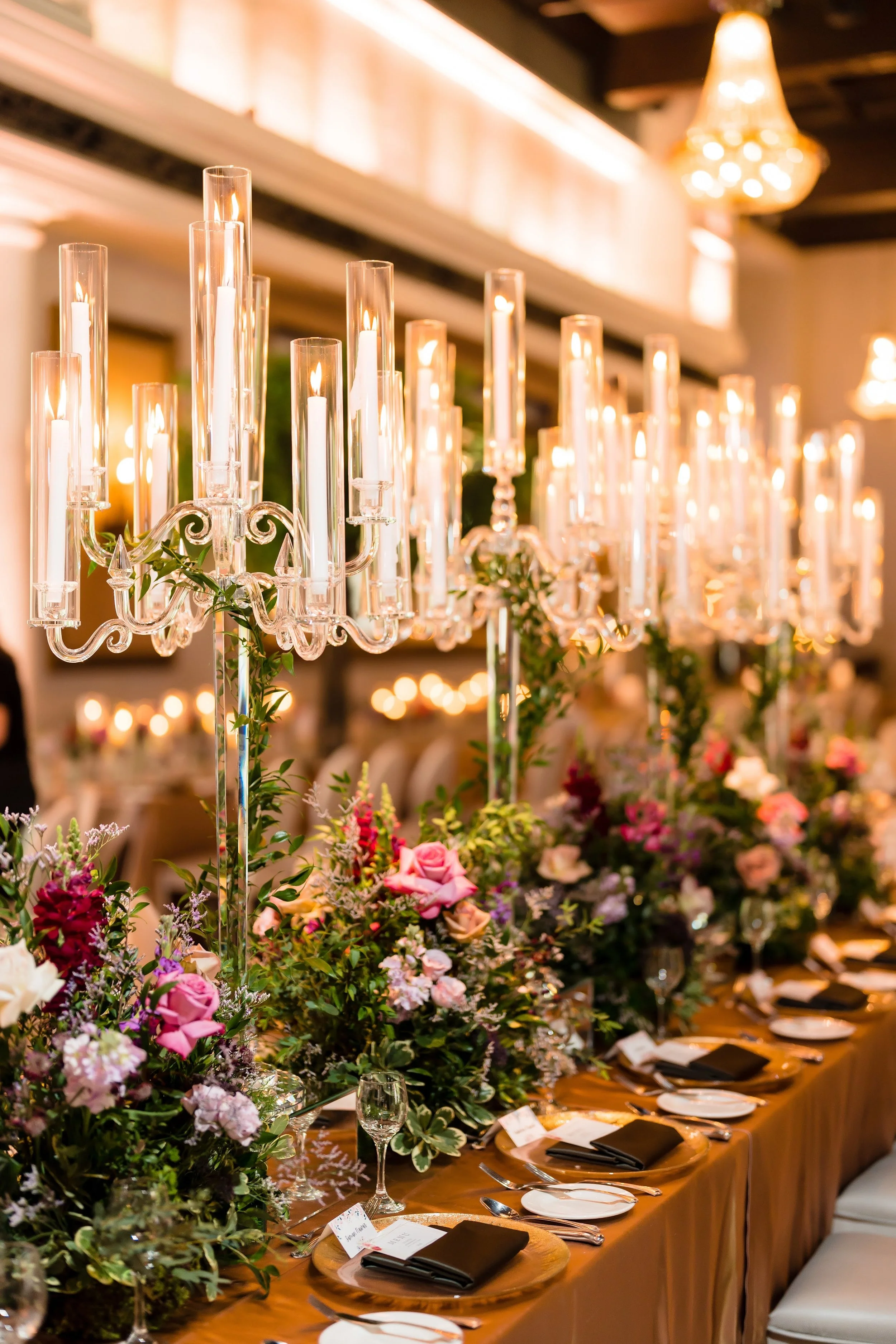 Elegant dining table with tall candelabra, candles, and colorful floral centerpieces at a formal event or wedding reception.