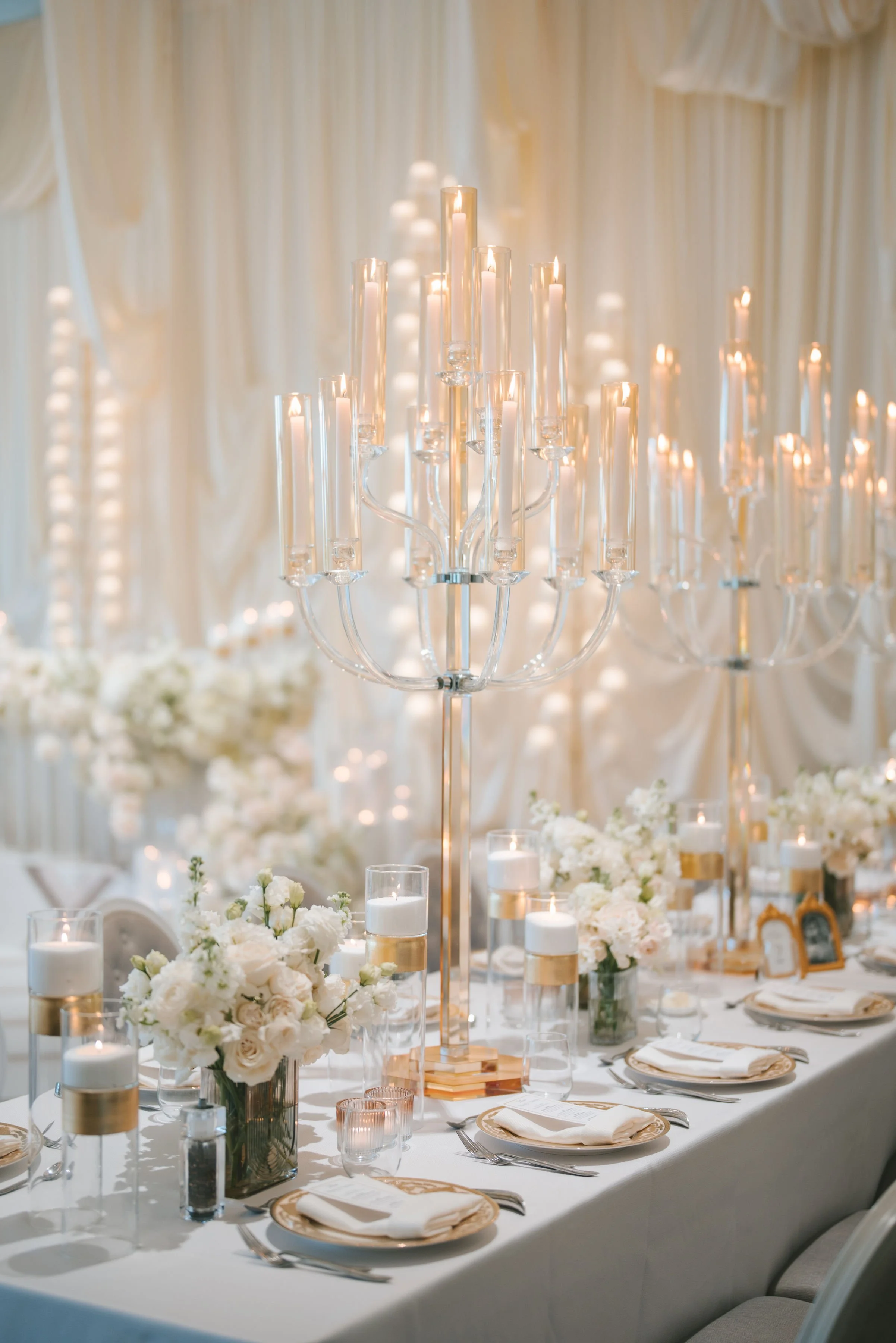 Elegant wedding reception table with white floral centerpieces, candles, and a large candelabrum with lit candles.