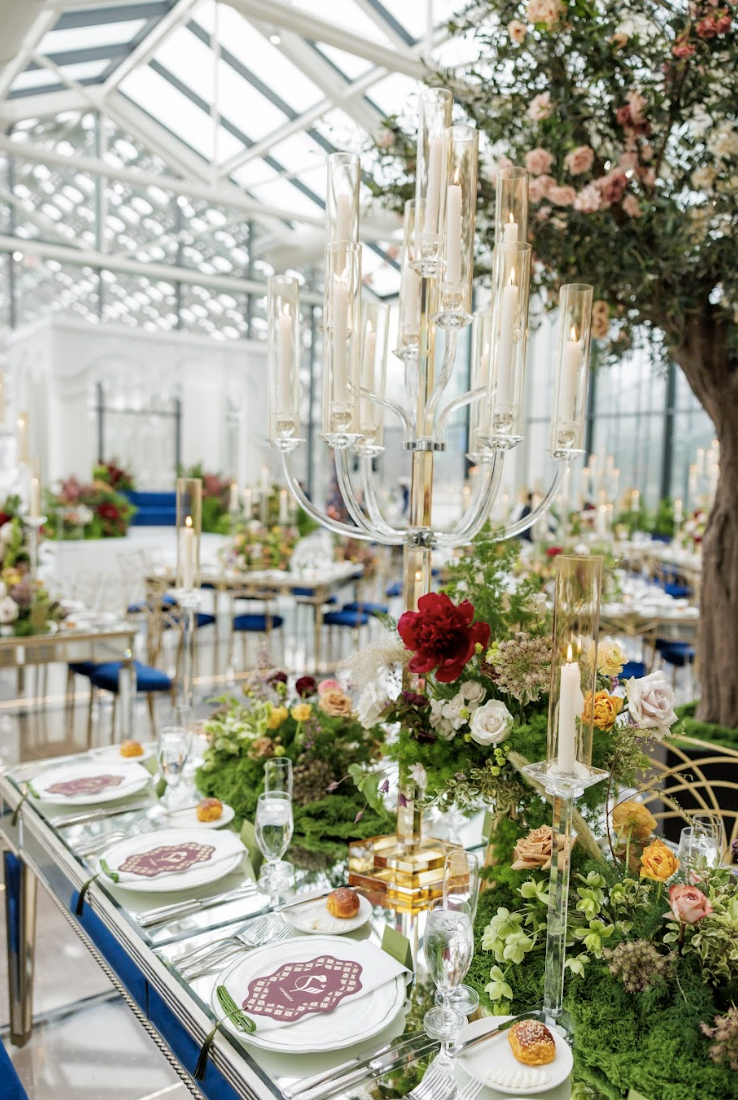 Elegant banquet table decorated with flowers, candles, and tableware in a glass-ceiling conservatory setting.