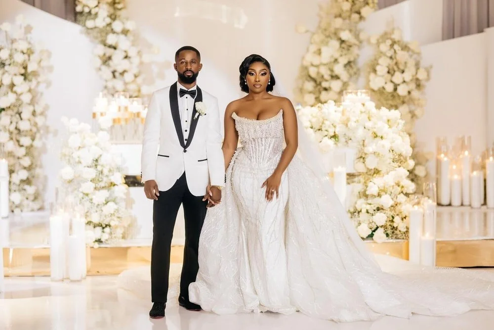 A bride and groom standing together in a decorated wedding venue with white flowers and lit candles.