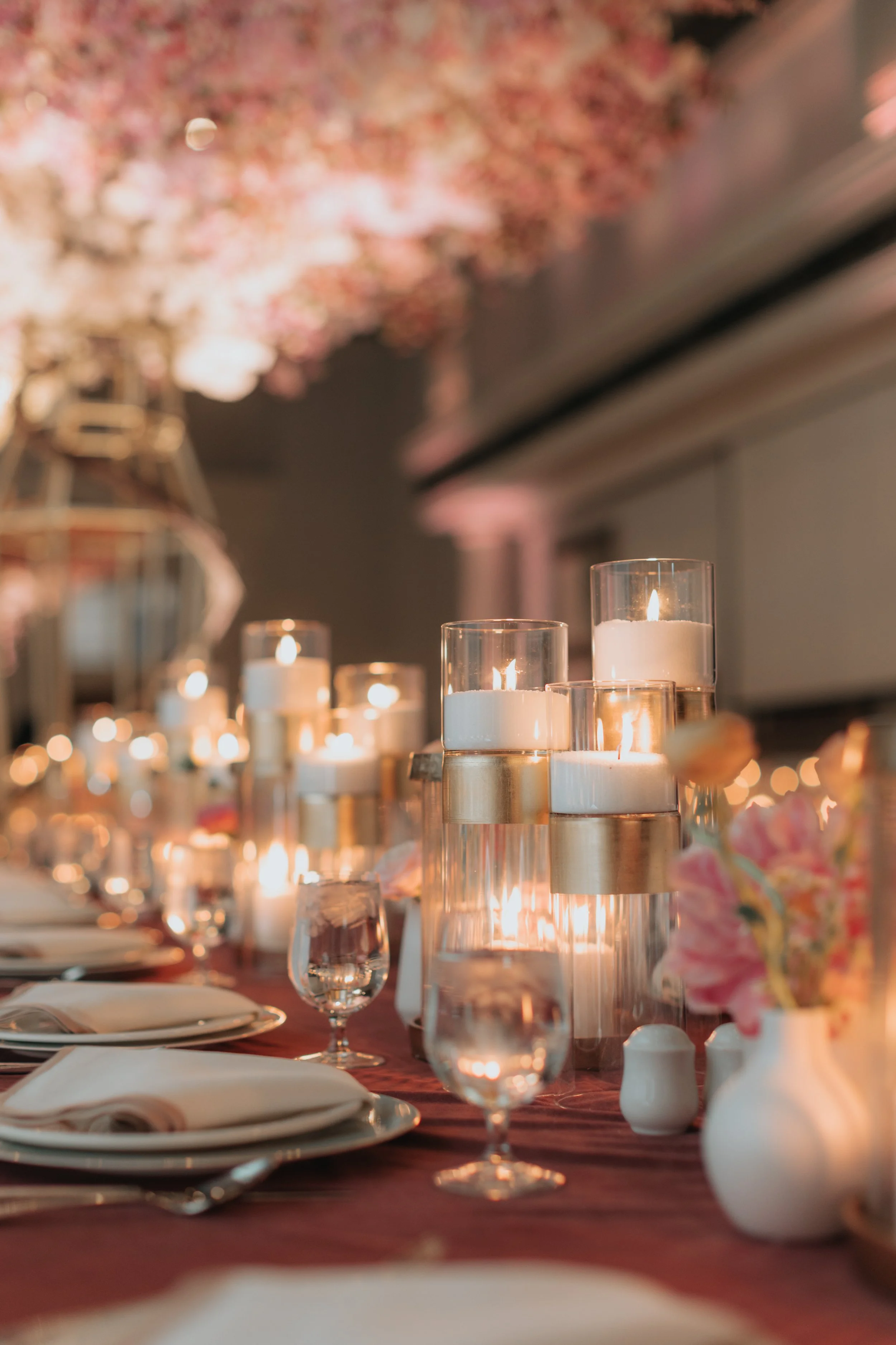 Elegant table setup with candles, wine glasses, floral arrangements, and dinnerware for a celebration or special event.