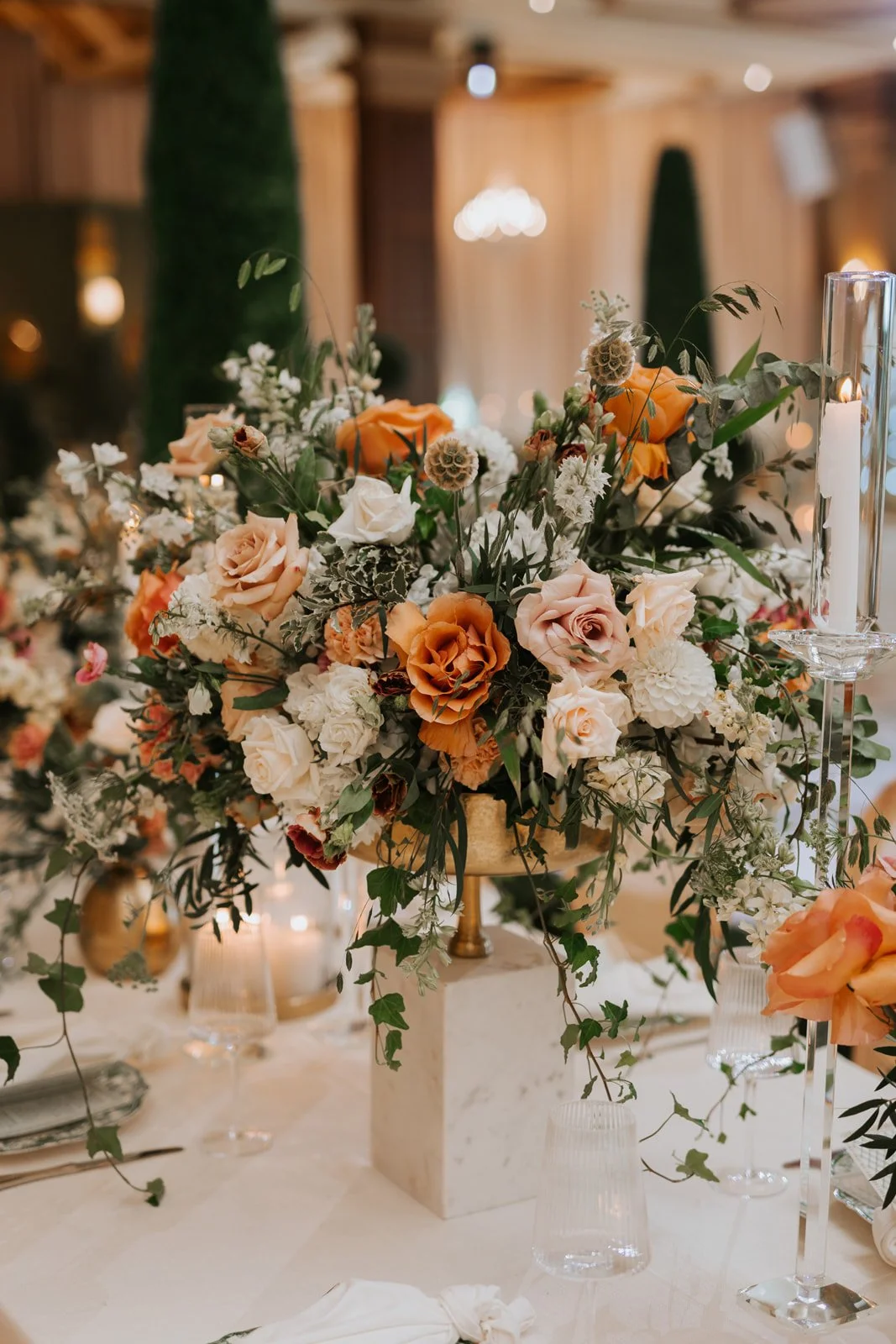 A floral centerpiece with peach and white roses, white dahlias, greenery, and decorative elements on a table.