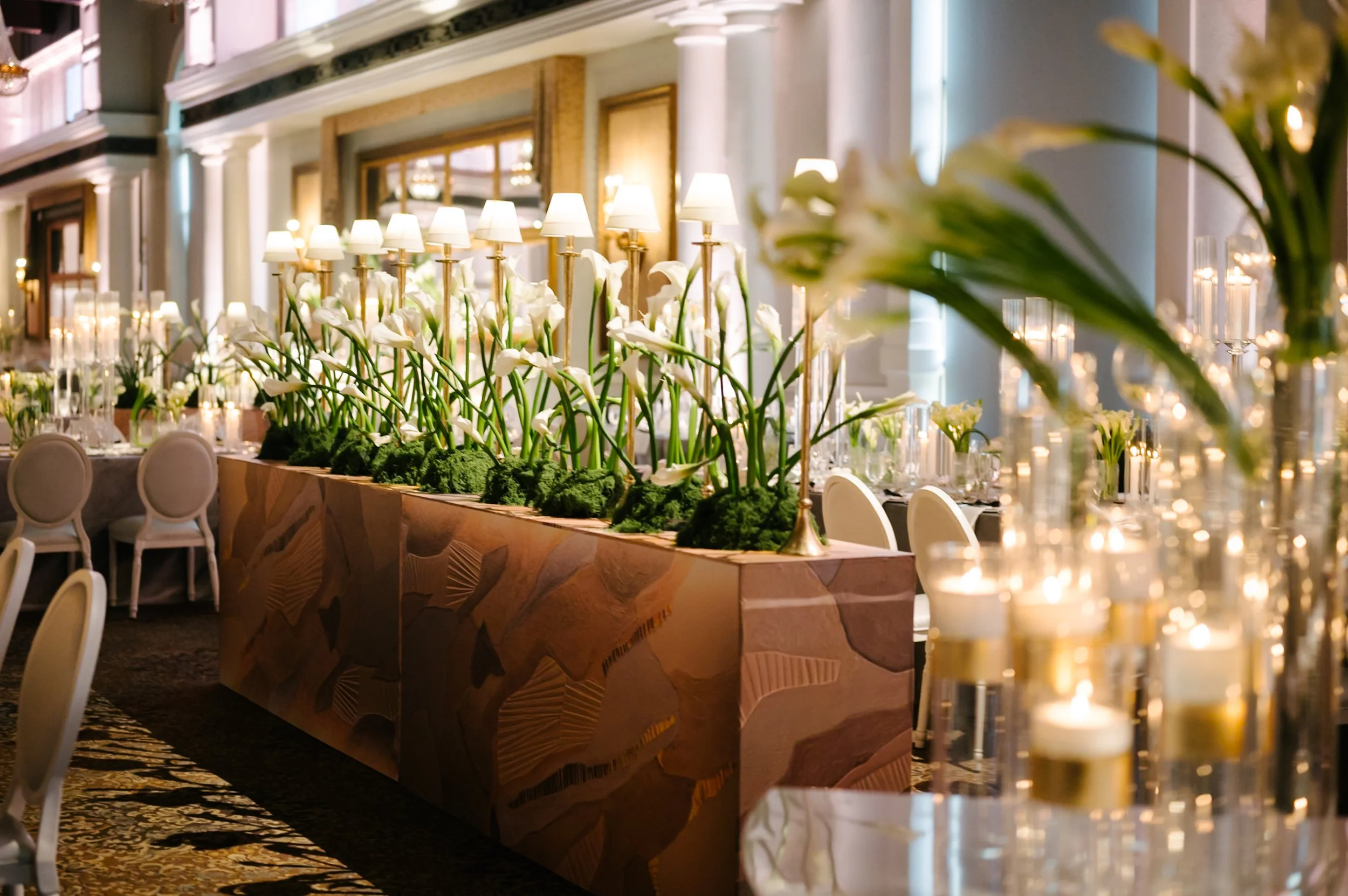 Elegant banquet hall decorated with white calla lilies and lit lamps, set for a formal event.