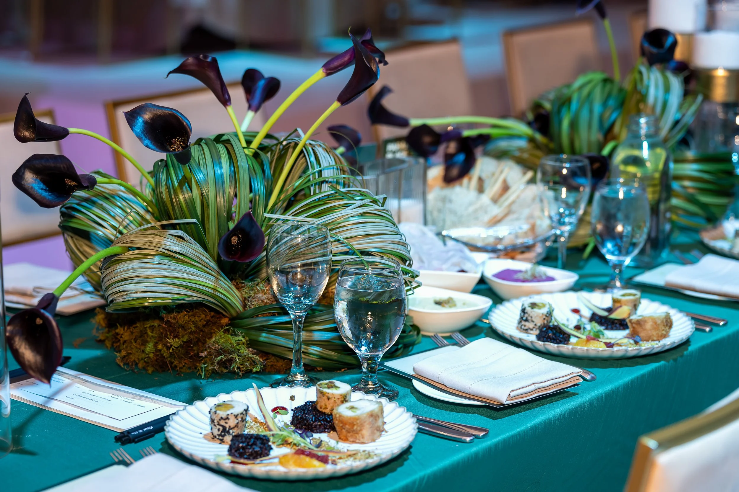 Architectural centrepieces — black calla lilies with sculptural looped grasses on an emerald table. Floral design by Ethereal Creators.
