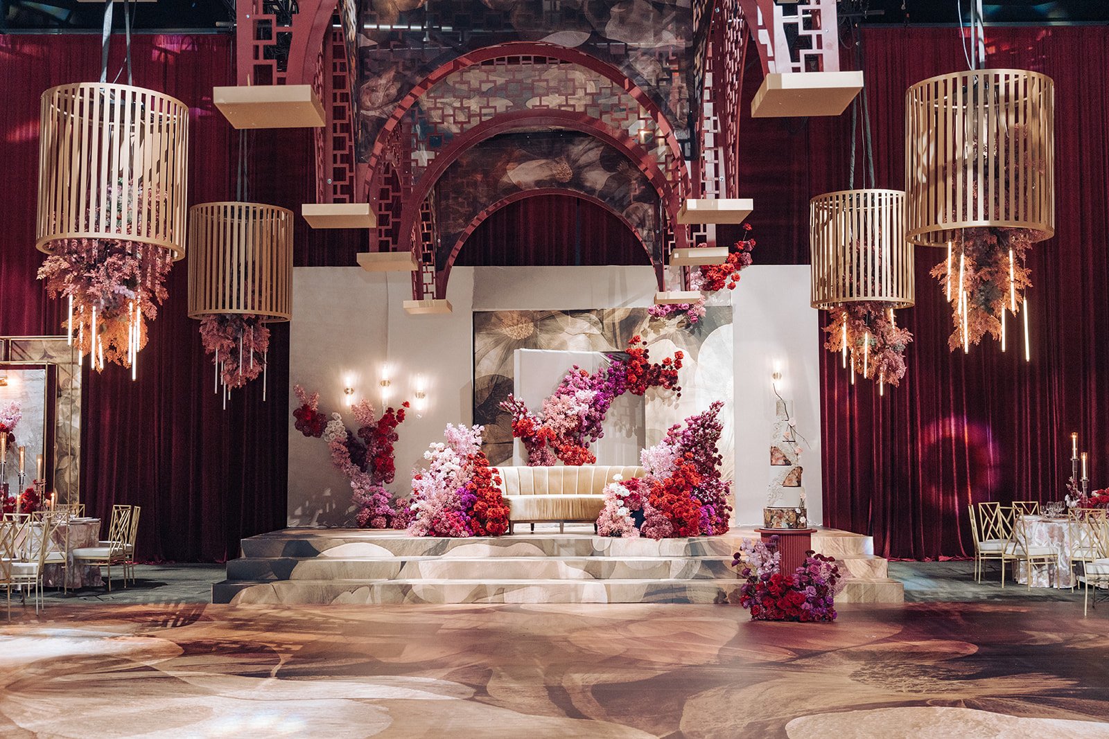 Grand red architectural wedding stage with gold cage chandeliers and cascading florals at Universal Event Space, by Ethereal Creators.