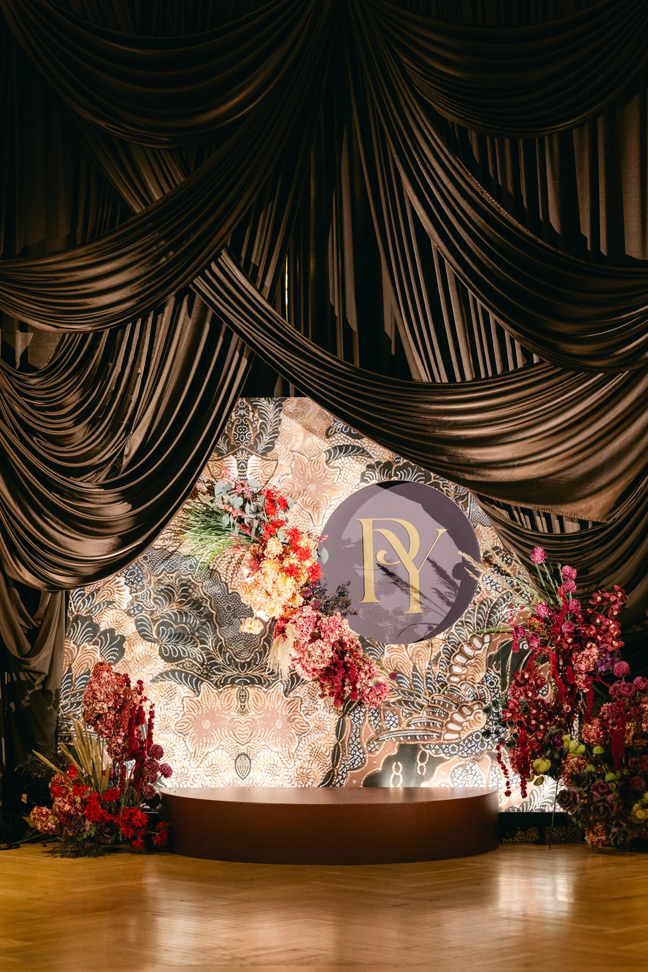 Elegant event stage with black drapes, floral arrangements, and a decorative backdrop featuring the initials RY in gold on a gray circle.