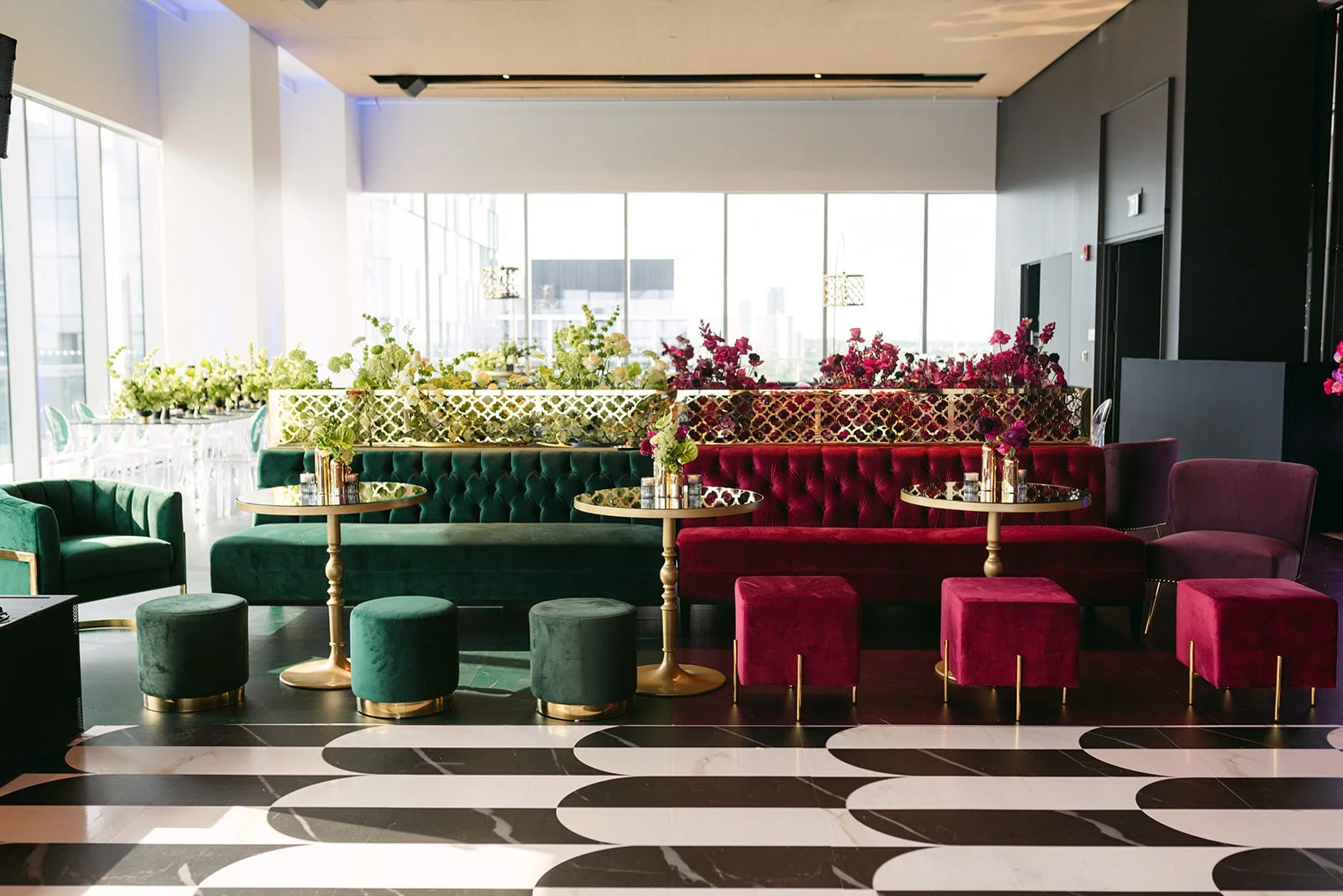 Luxurious hotel lobby with green and red velvet seating, gold accents, and floral arrangements, large windows in the background.