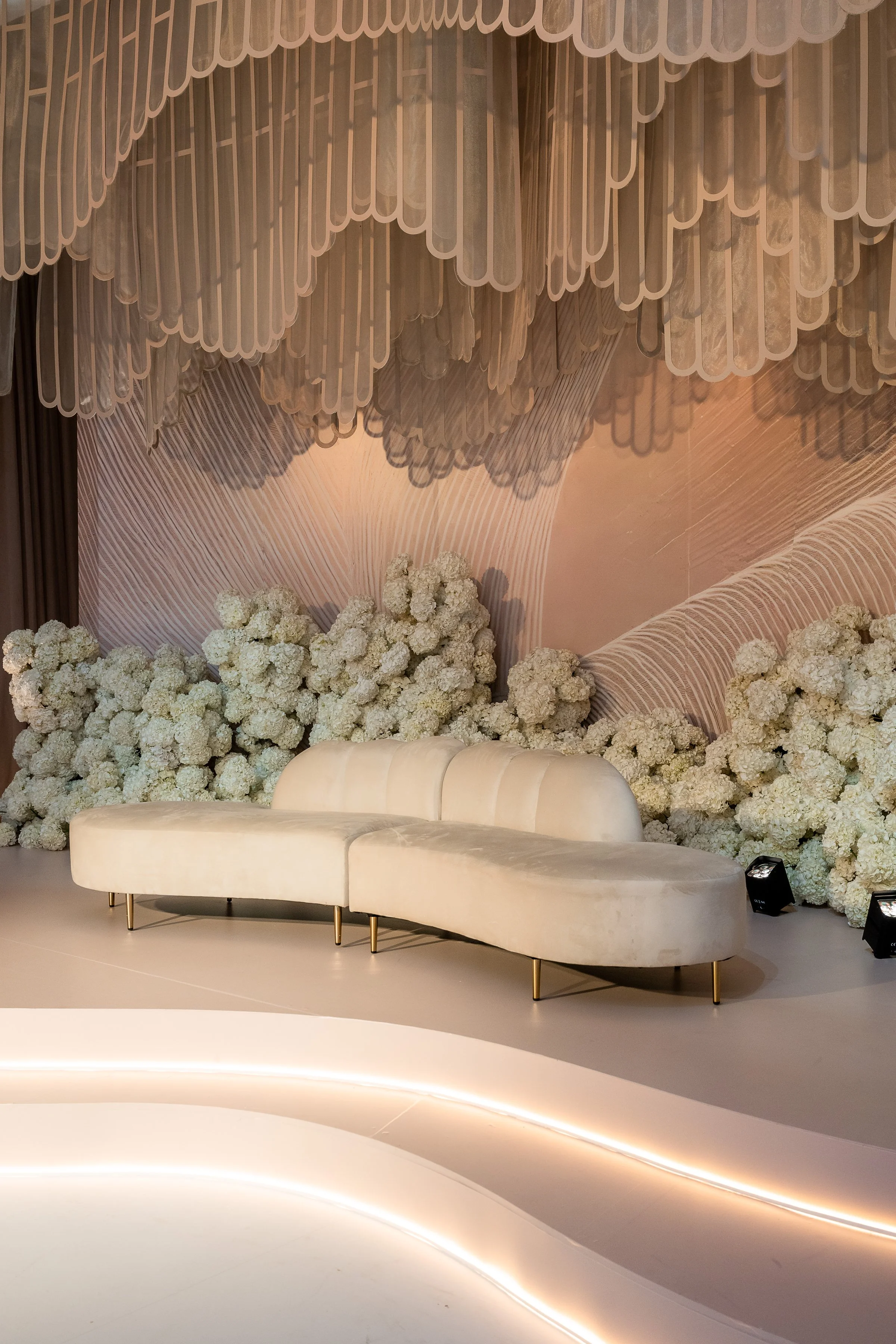All-white Kabbalat Panim room with a laser-cut swirl ceiling installation, white hydrangea and an ivory velvet love seat, designed by Ethereal Creators.