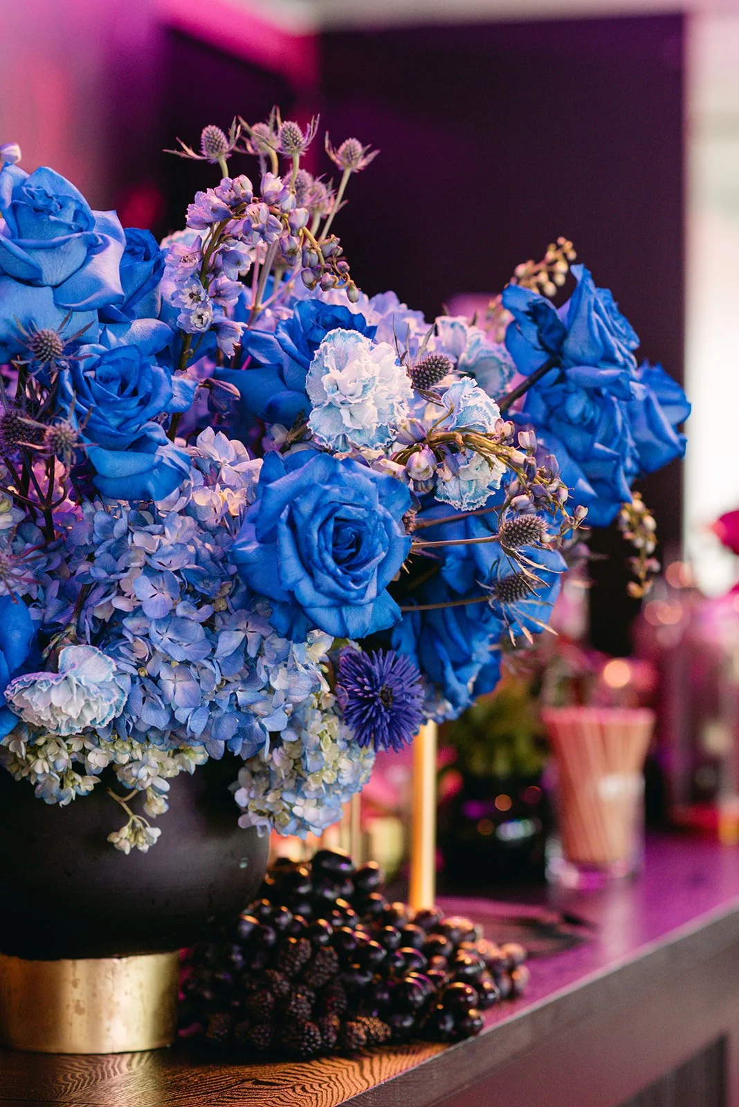 A colorful floral arrangement with blue roses, hydrangeas, and other flowers in a black and gold vase on a table.
