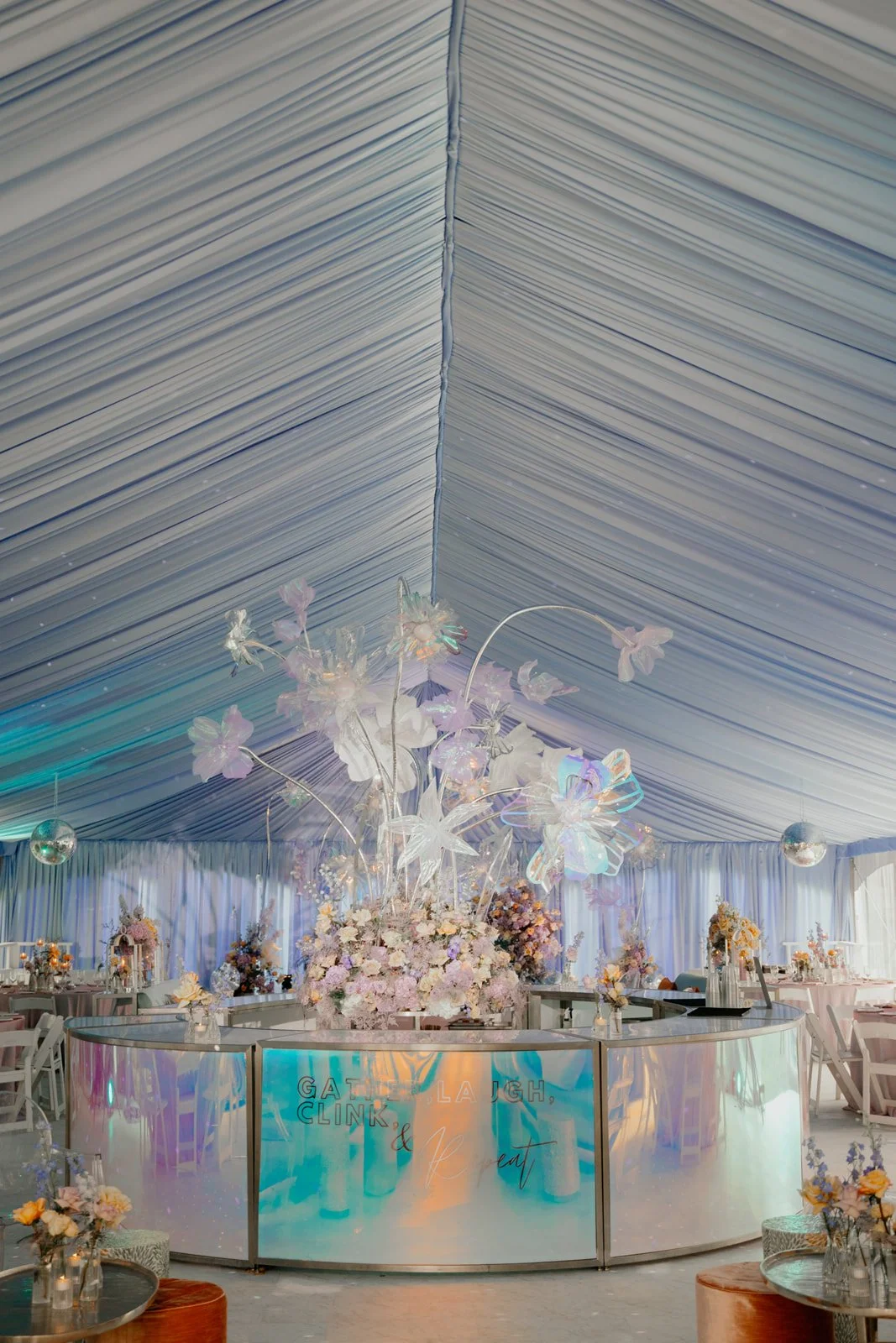 Decorated event venue with iridescent floral centerpiece, draped ceiling, and seating arrangements.