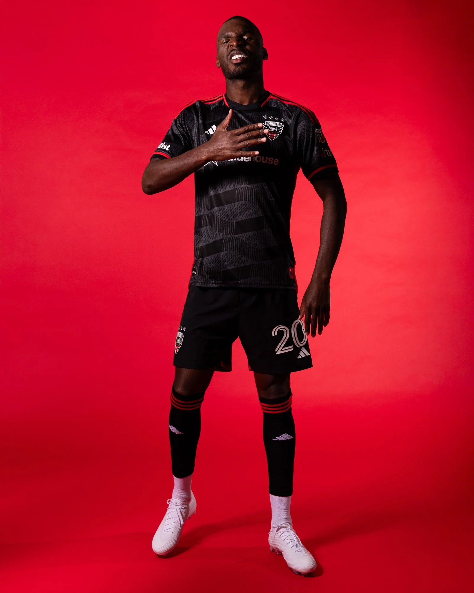 D.C. United forward Christian Benteke poses during the club’s 2025 media day, striking a celebratory stance while hitting his chest and reacting toward the camera on a red backdrop. (Cody Cervenka/Crvnka Photography)