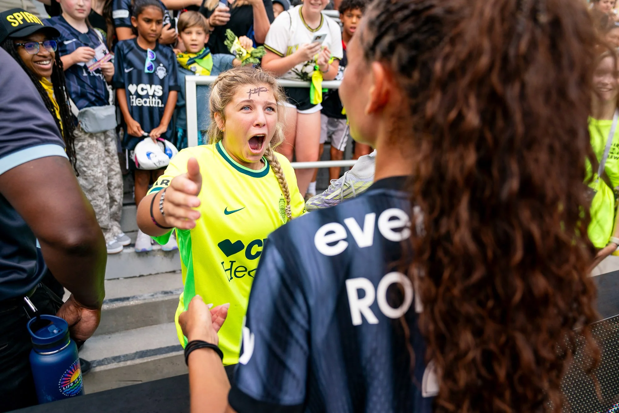 Washington Spirit forward Trinity Rodman signs the forehead of a young fan and hands over one of her cleats following a match against the Portland Thorns. The image is captured over Rodman’s shoulder, showing the fan’s surprised reaction as the cleat