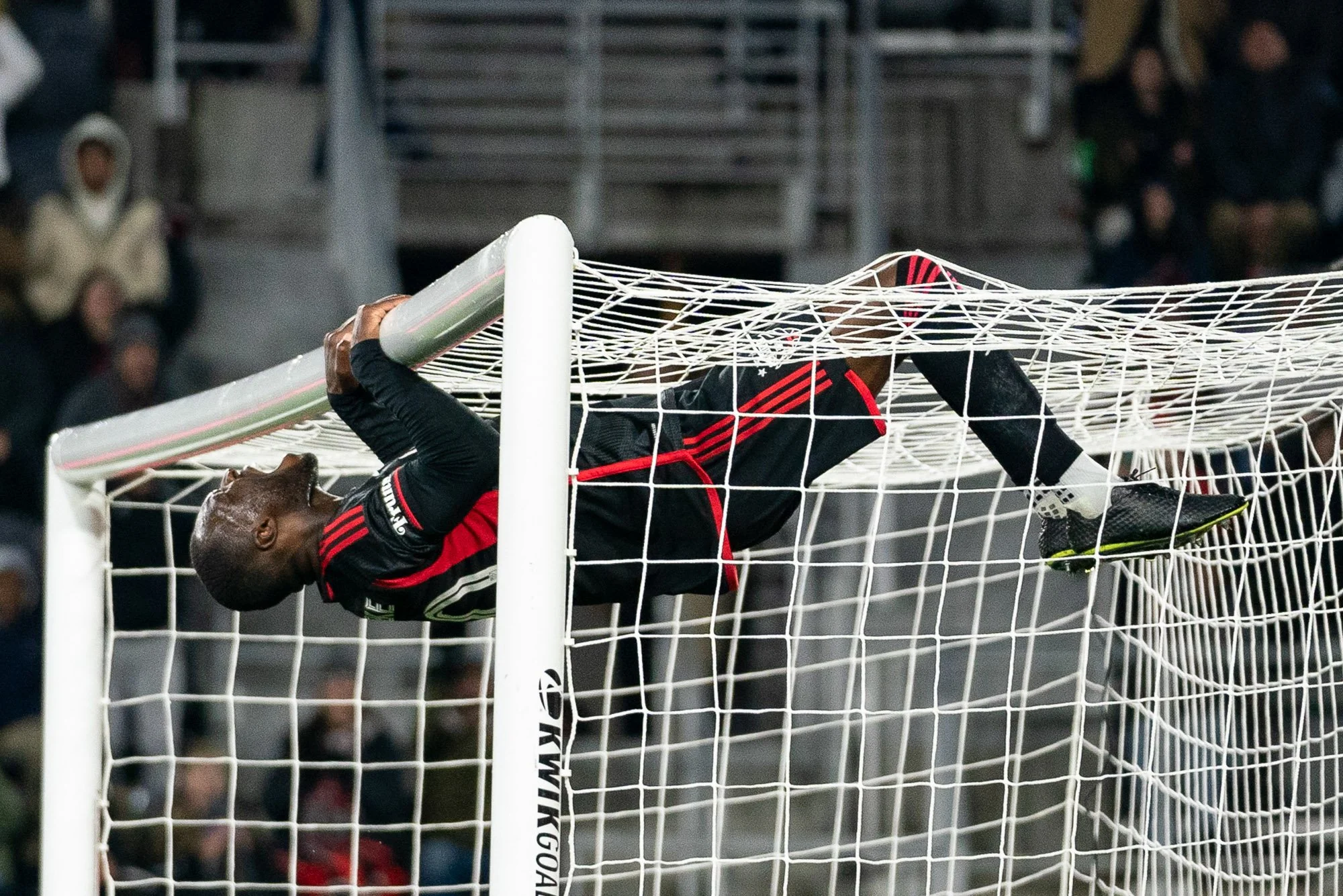 D.C. United forward Christian Benteke reacts after a missed scoring opportunity during a 2024 MLS match against the New England Revolution, swinging on the crossbar parallel with the ground and shouting in frustration. (Cody Cervenka/Crvnka Photograp