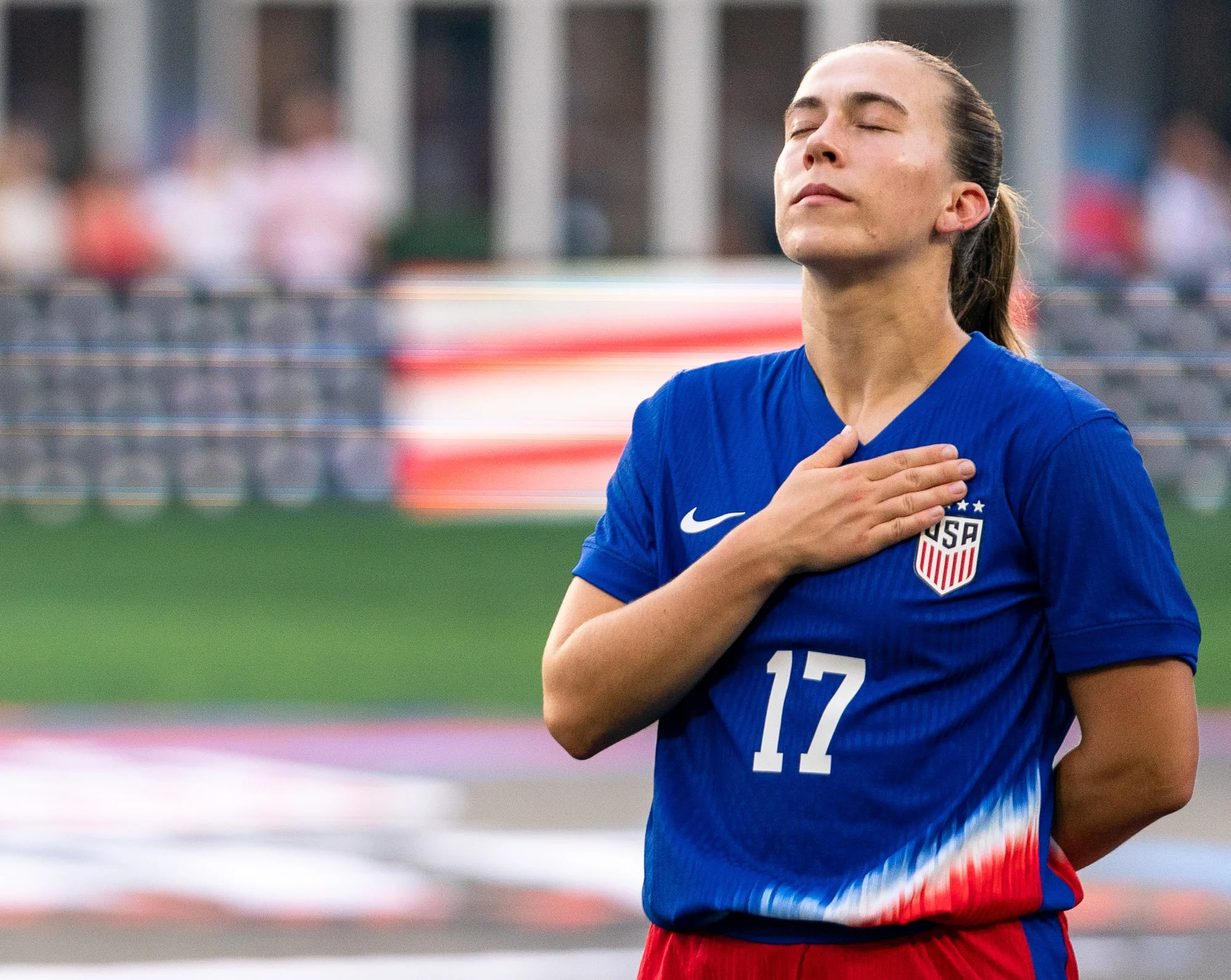 United States midfielder Sam Coffey stands with her hand over her heart during the national anthem prior to an international friendly against Costa Rica at Audi Field. The American flag is displayed on the stadium video board behind her. (Cody Cerven