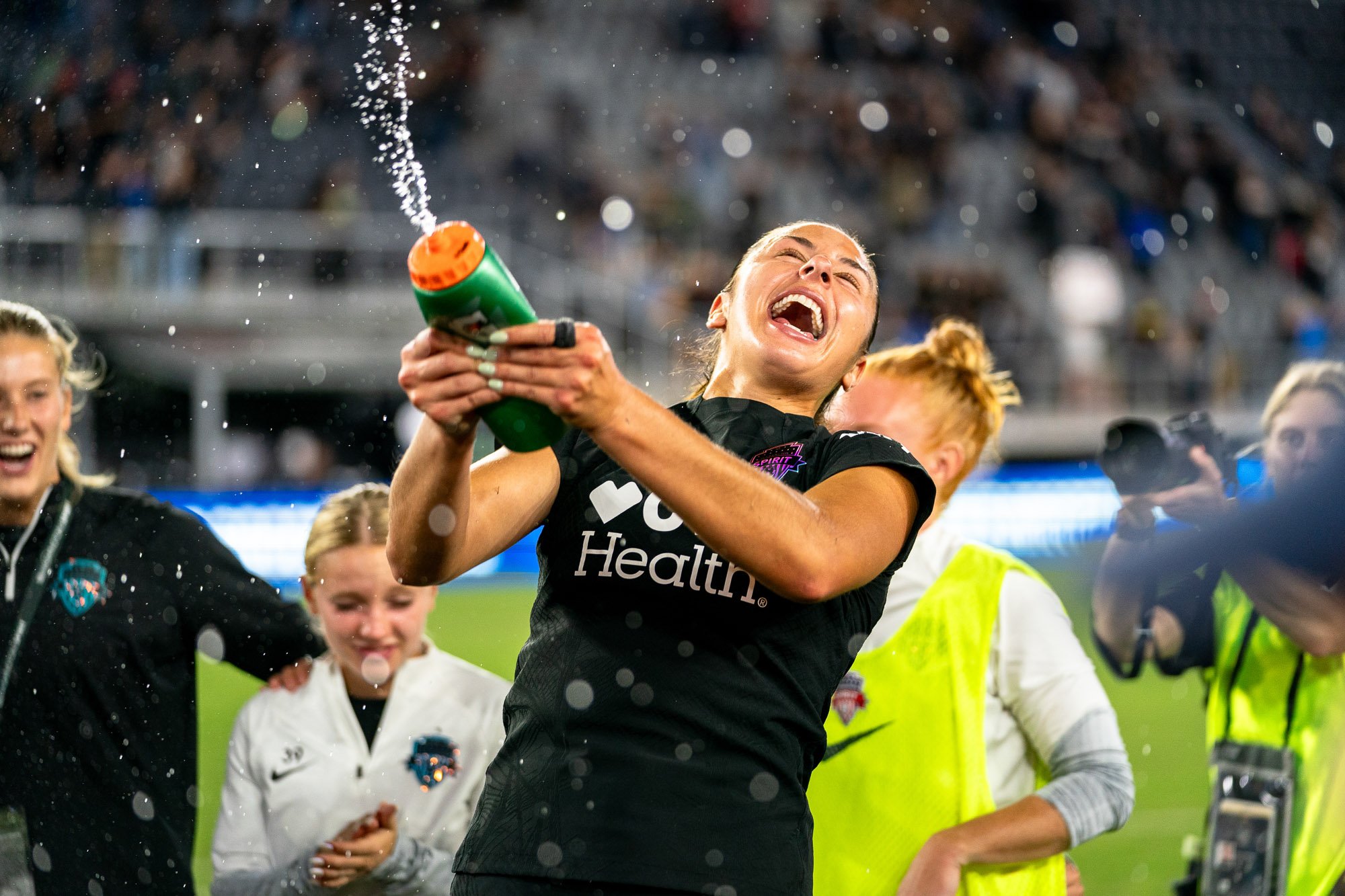 Washington Spirit defender Sam Staab celebrates in a post-game huddle after a match against the Kansas City Current at Audi Field, smiling as she sprays water into the air following the final whistle. (Cody Cervenka/Crvnka Photography)