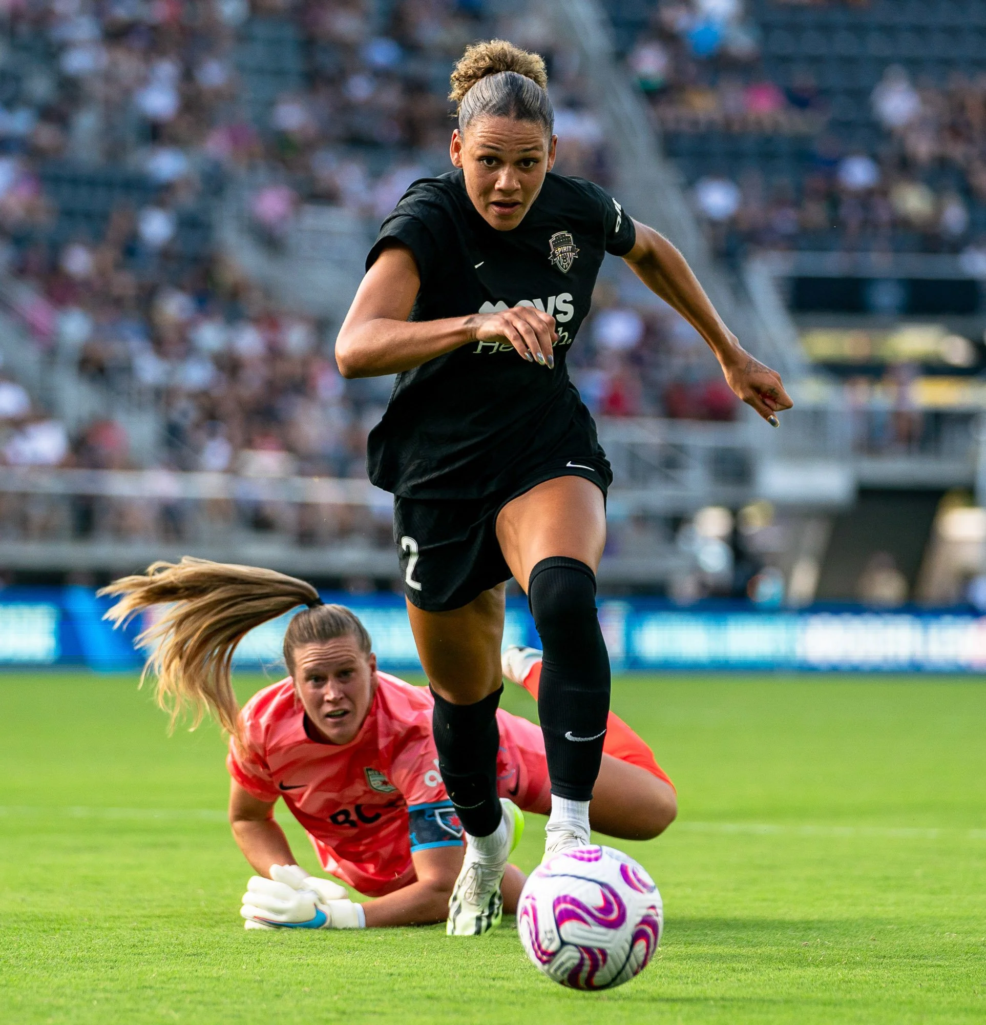 Washington Spirit forward Trinity Rodman dribbles past Chicago Stars FC goalkeeper Alyssa Naeher during a match, chasing the ball as it rolls toward the camera while Naeher twists on the ground after being beaten on the play. The moment came shortly 