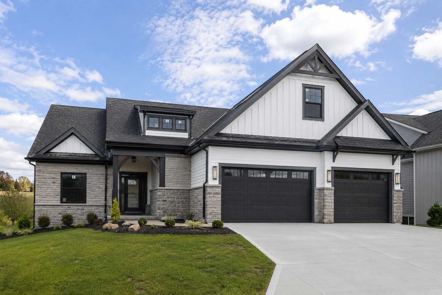 Modern two-story house with black garage doors, white siding, stone and wood exterior, front porch, landscaped lawn, and a cloudy sky.