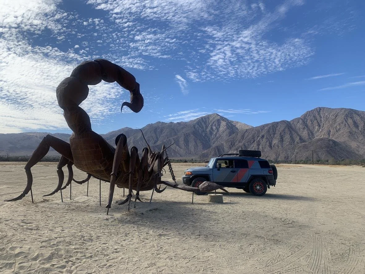Giant metal scorpion statue in the desert with a Toyota FJ