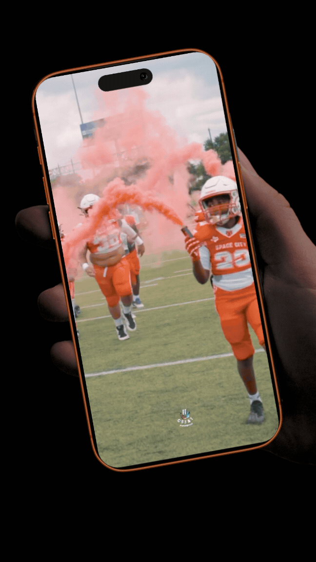 Football players running onto the field through a cloud of pink smoke, with one player holding a pink smoke flare.
