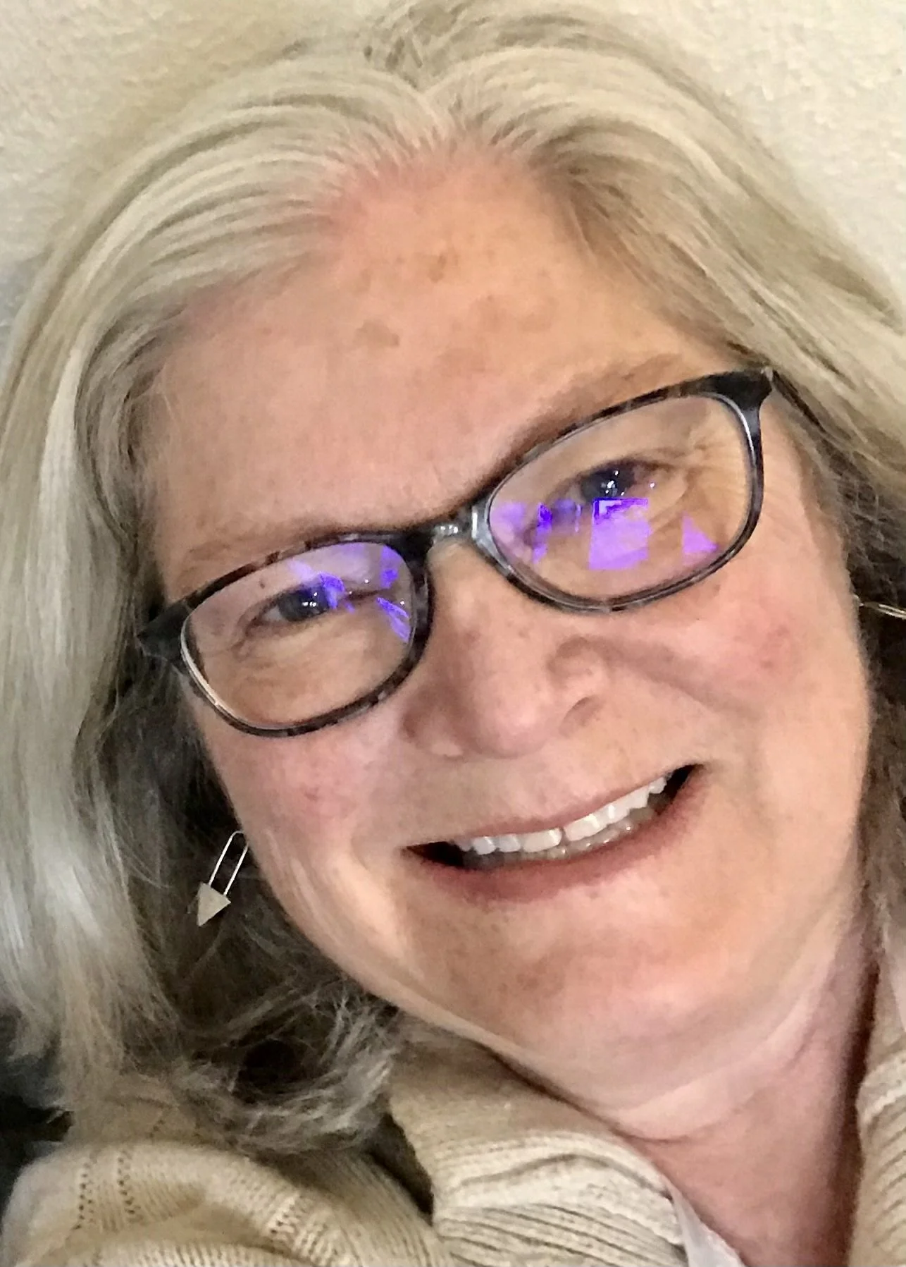 Close-up of an elderly woman with gray hair, glasses, and earrings, smiling.