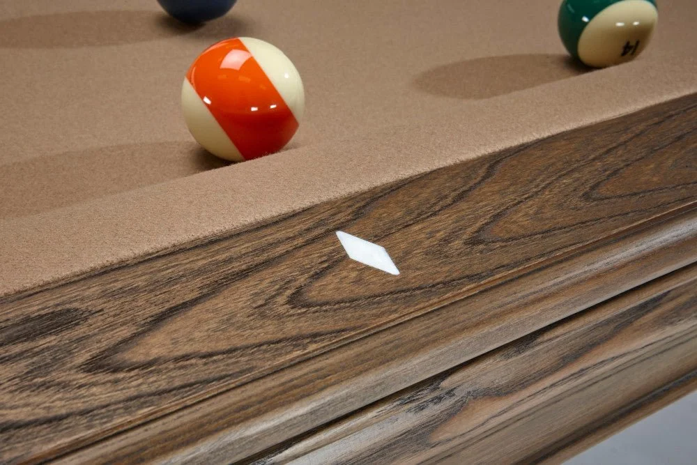 Close-up of a pool table with a cue ball and other balls, showing a white ball mark or sticker on the wooden edge of the table.