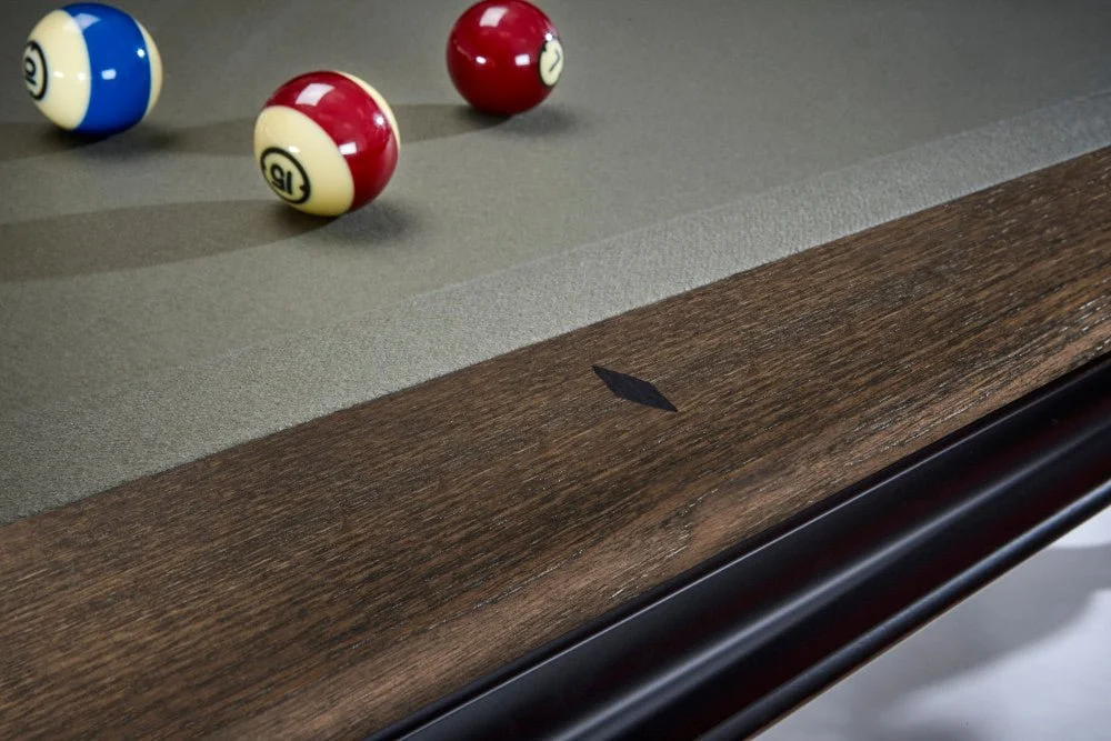 Close-up of a billiards table with a wood border, pool balls, and a cue stick holder.