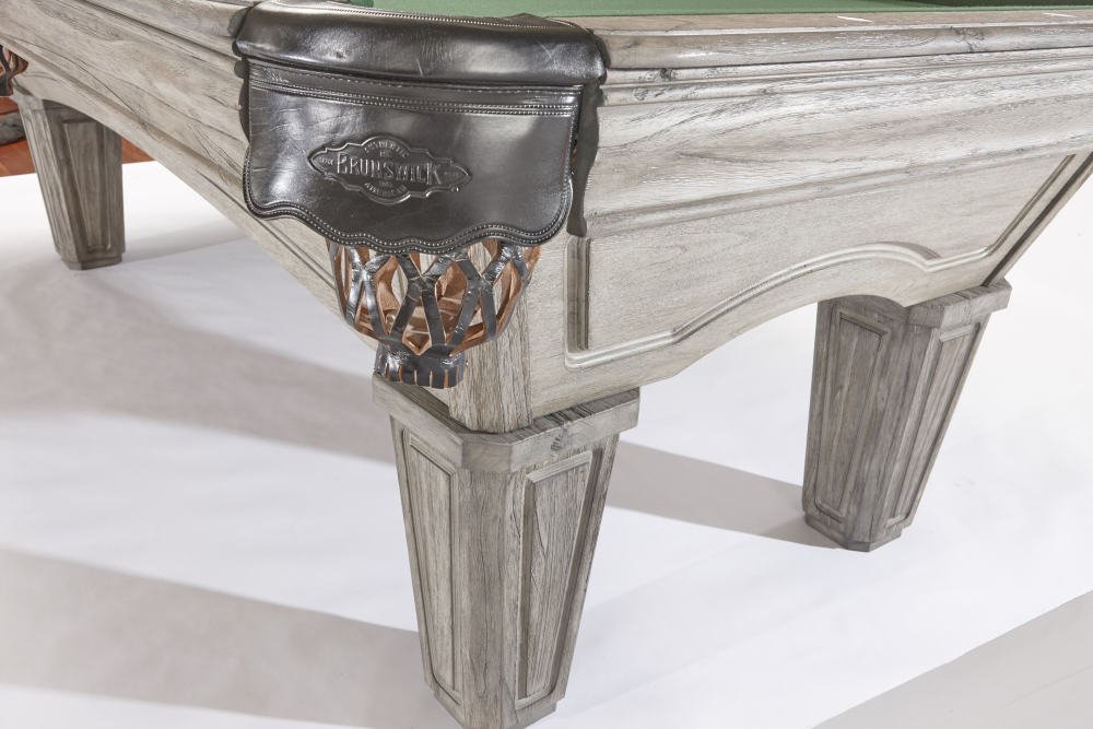 Close-up of a wooden pool table with a leather stick holder hanging on the corner, showing the corner and leg of the table.